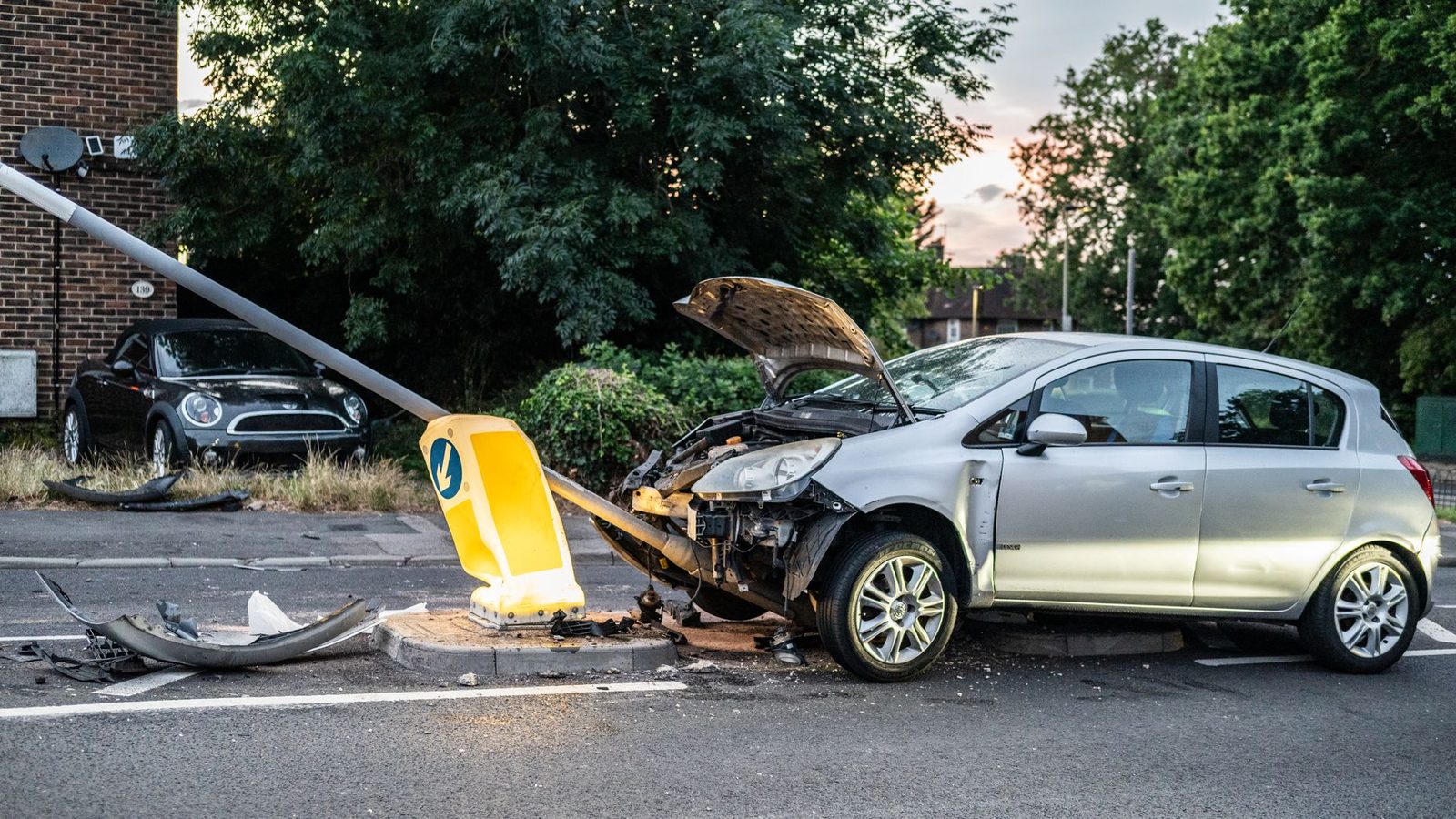 Auto dañado tras colisión contra poste de luz en calle urbana al atardecer.