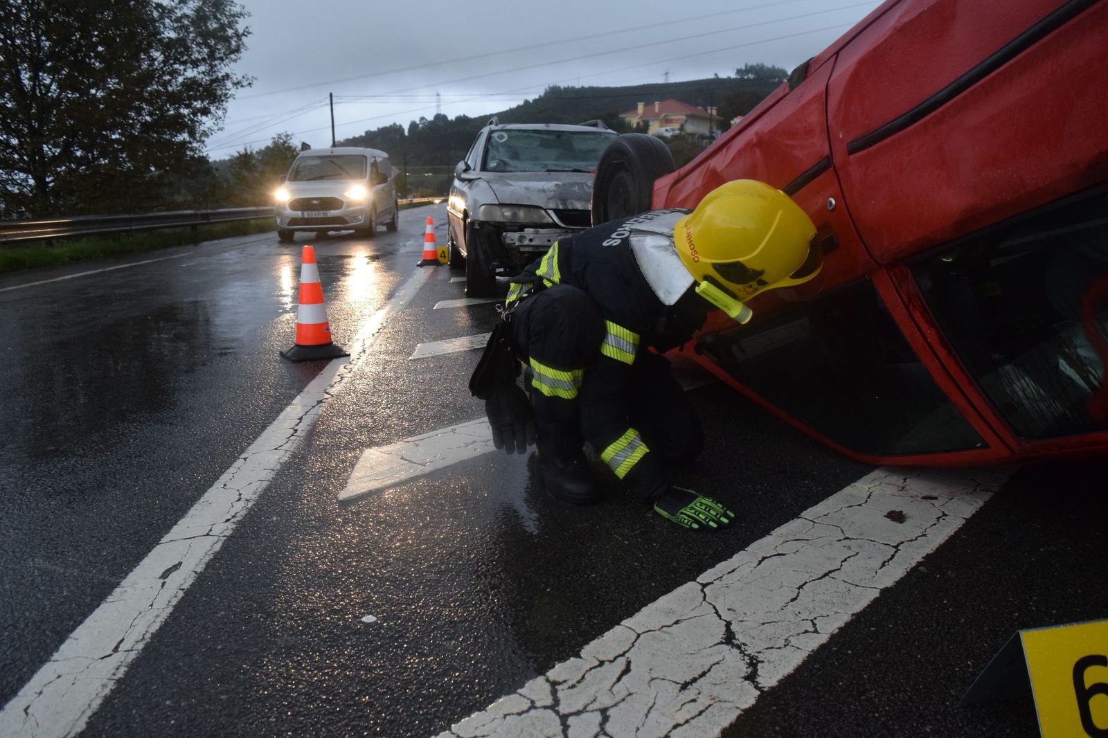 Bombero atendiendo automóvil volcado en carretera mojada durante lluvia.