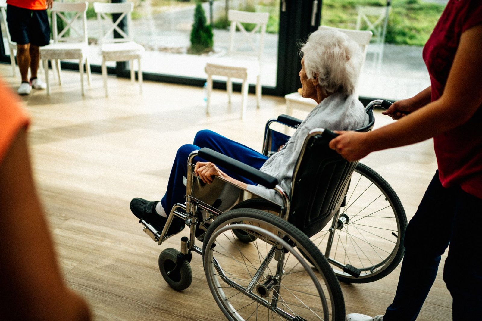 Caregiver assisting elderly patient in wheelchair at nursing home facility.