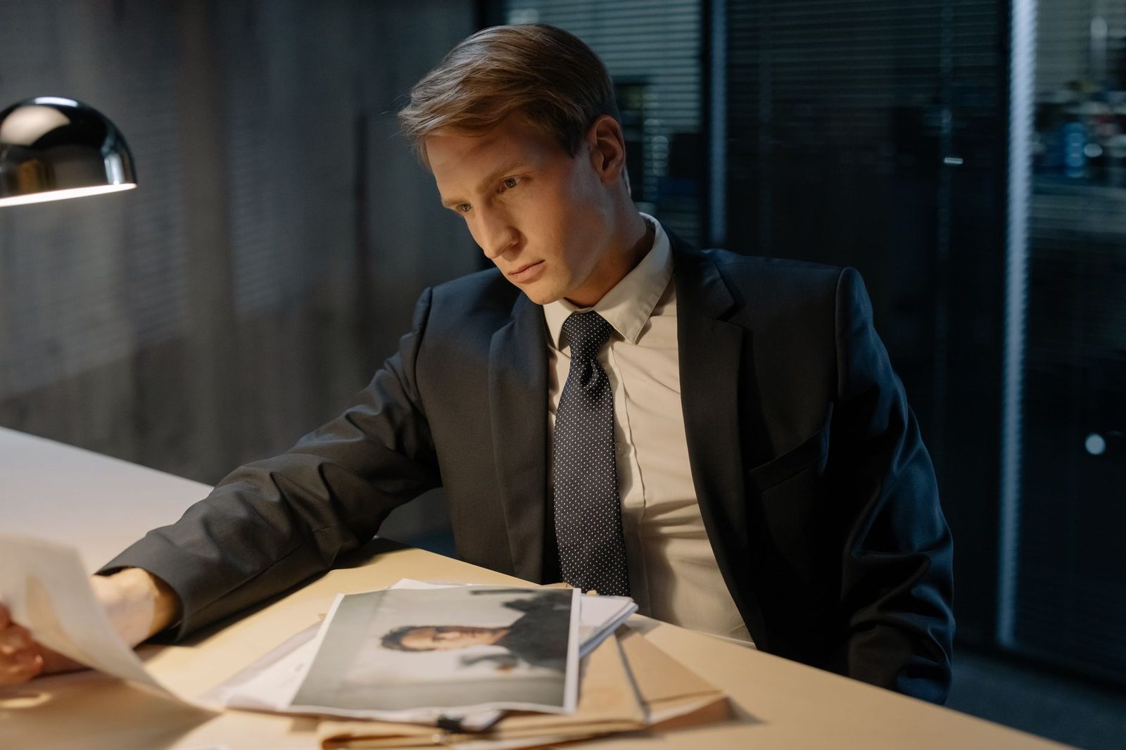 Detective reviewing case documents at desk under lamp light.