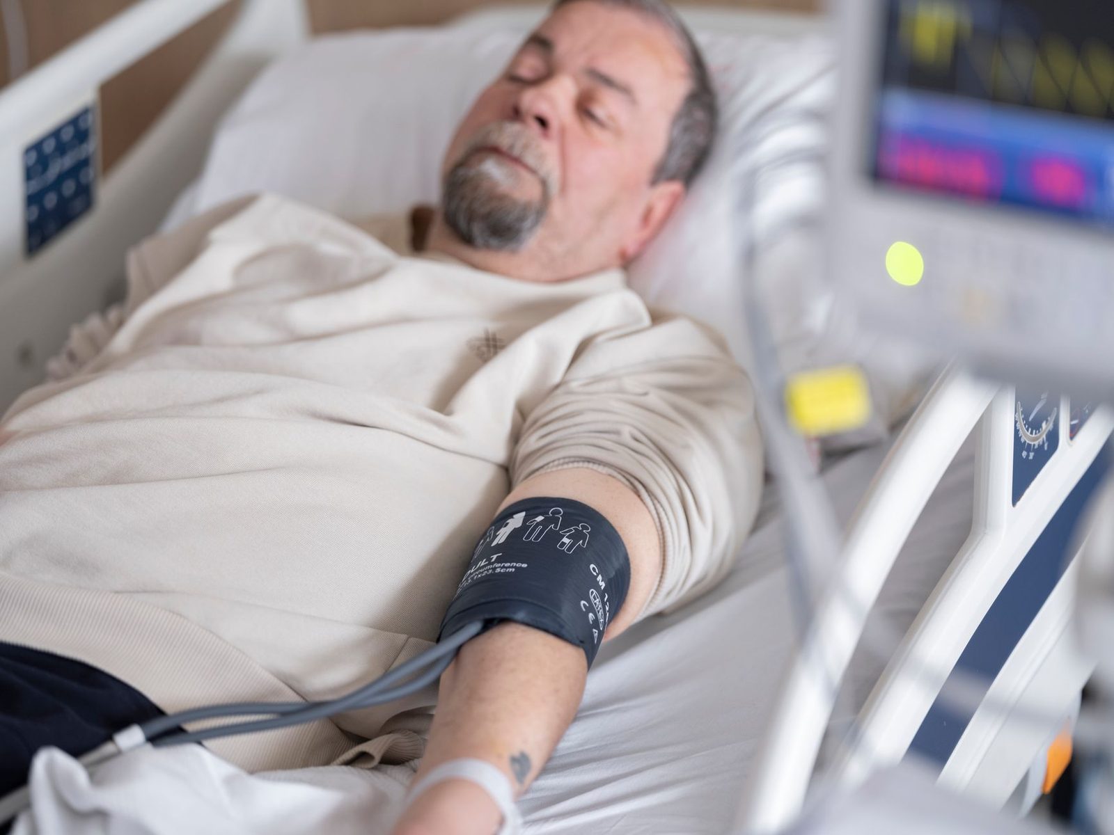 Elderly patient in hospital bed with blood pressure monitor.