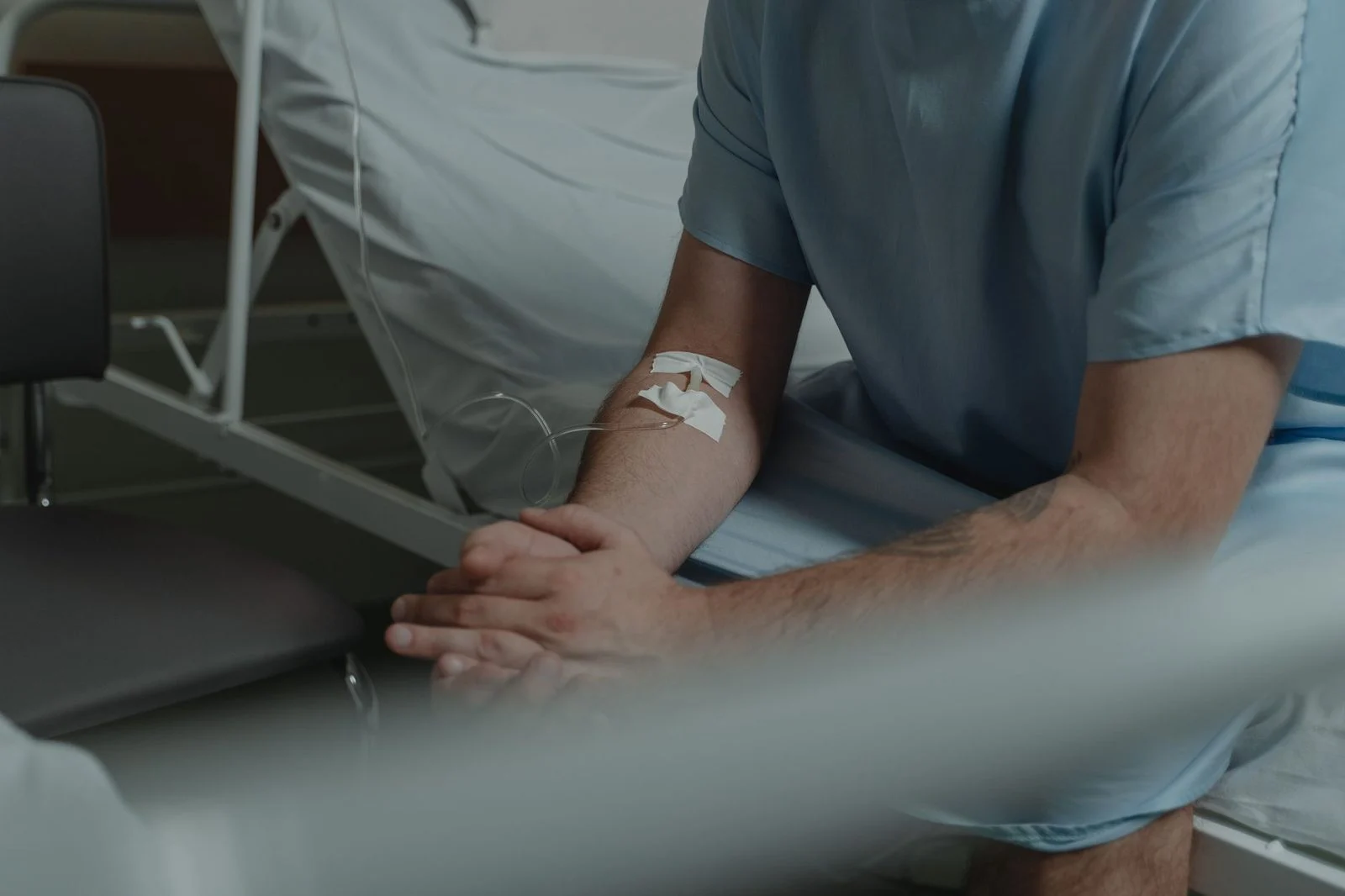 Elderly patient in hospital gown sitting on bed with IV line.