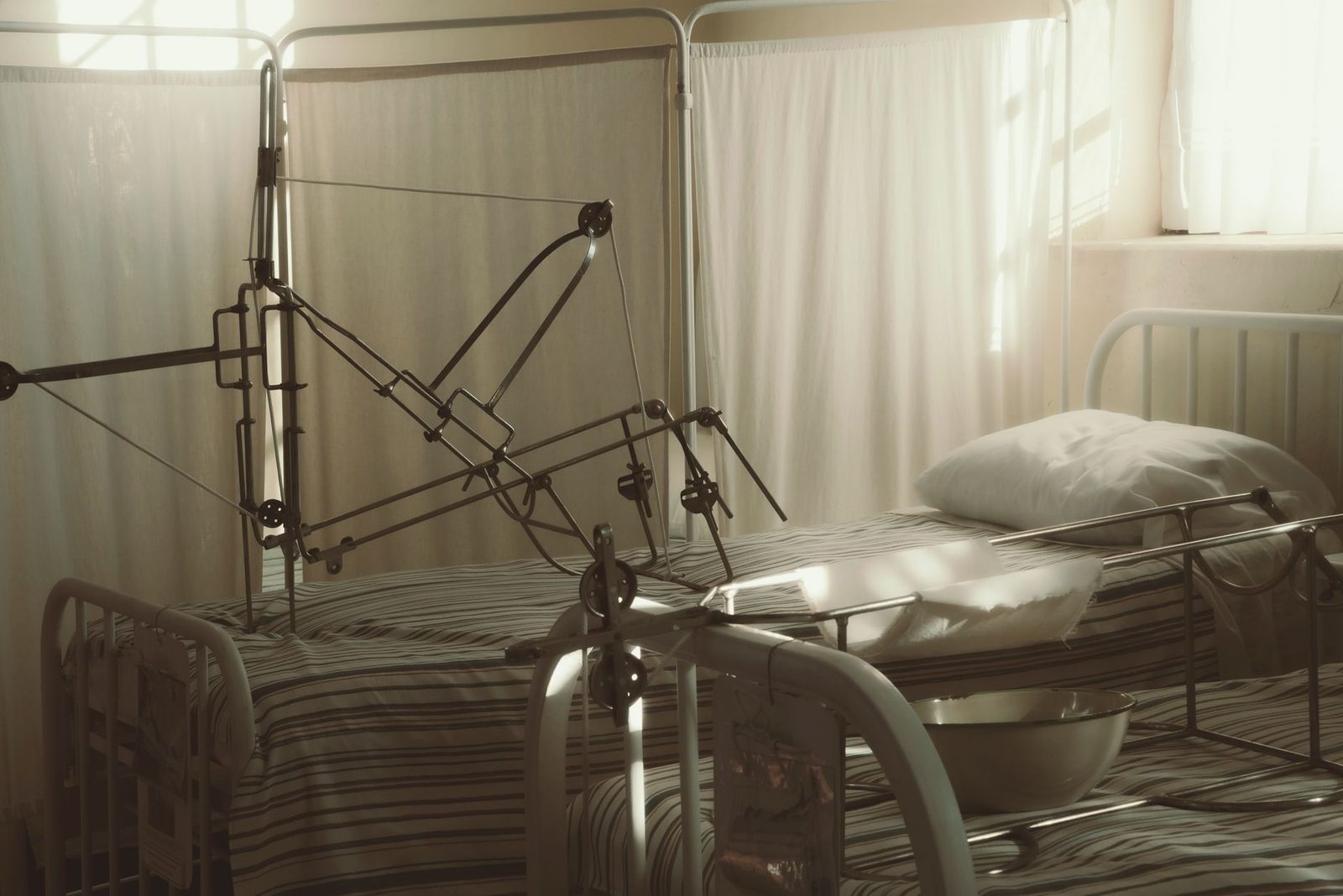 Empty hospital bed with medical equipment in sunlit room.