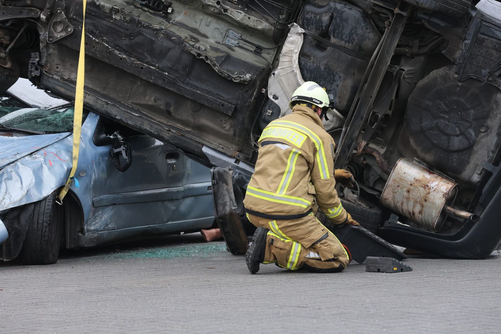 Firefighter in protective gear assisting at an overturned vehicle crash scene.