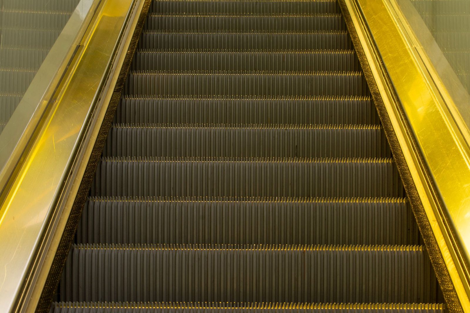 Golden escalator steps with metallic handrail in indoor setting.