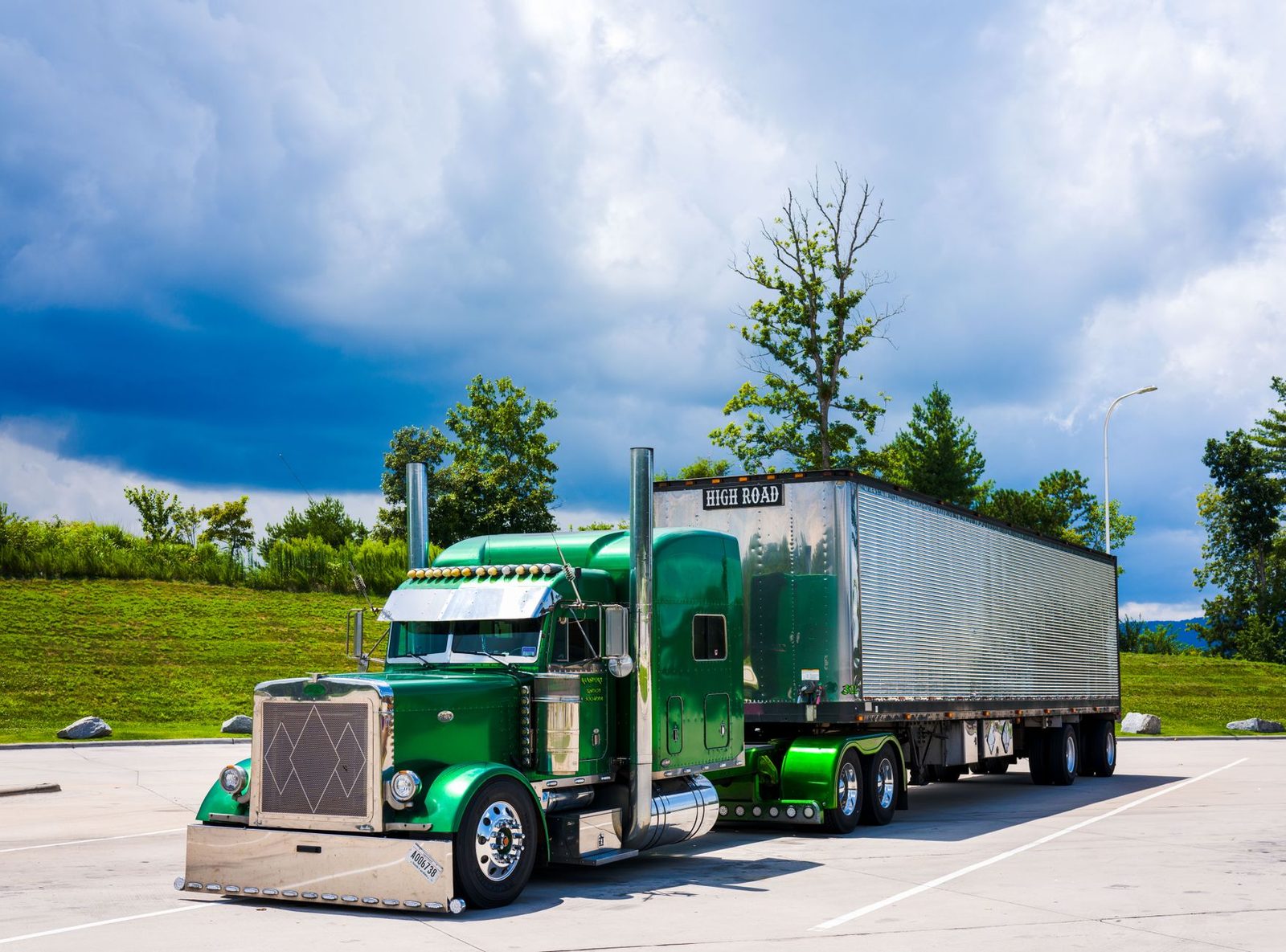 Green semi-truck parked with dramatic cloudy sky.