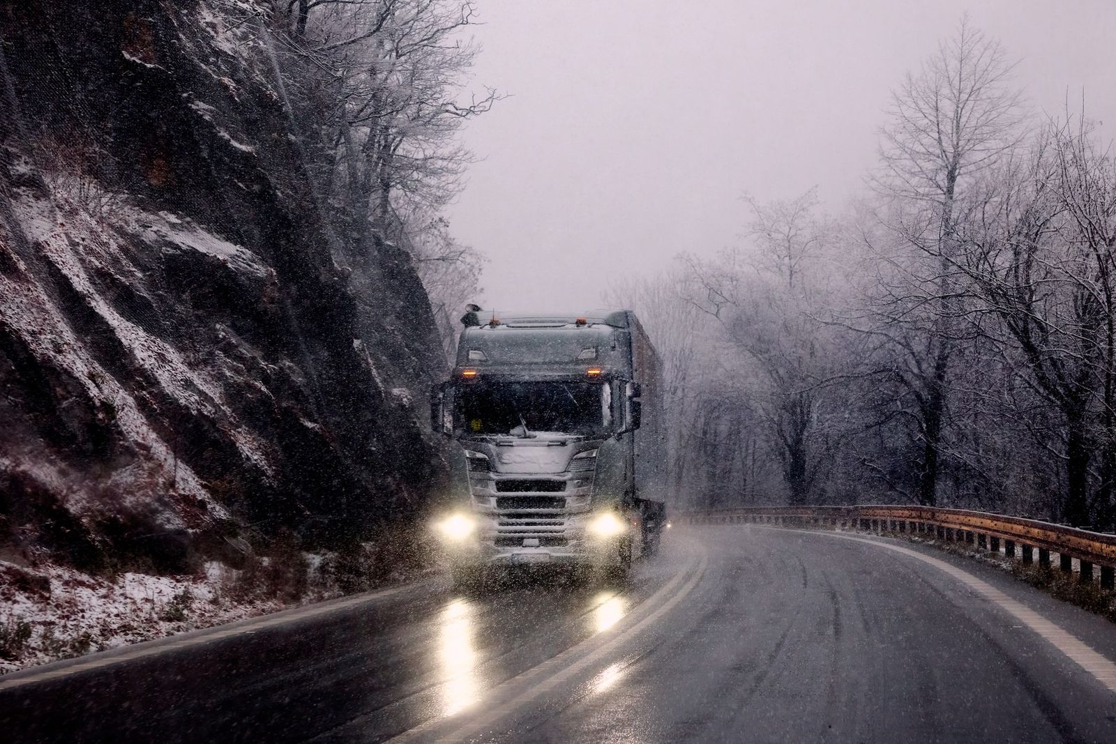 Heavy truck driving on snowy mountain road during winter snowfall.