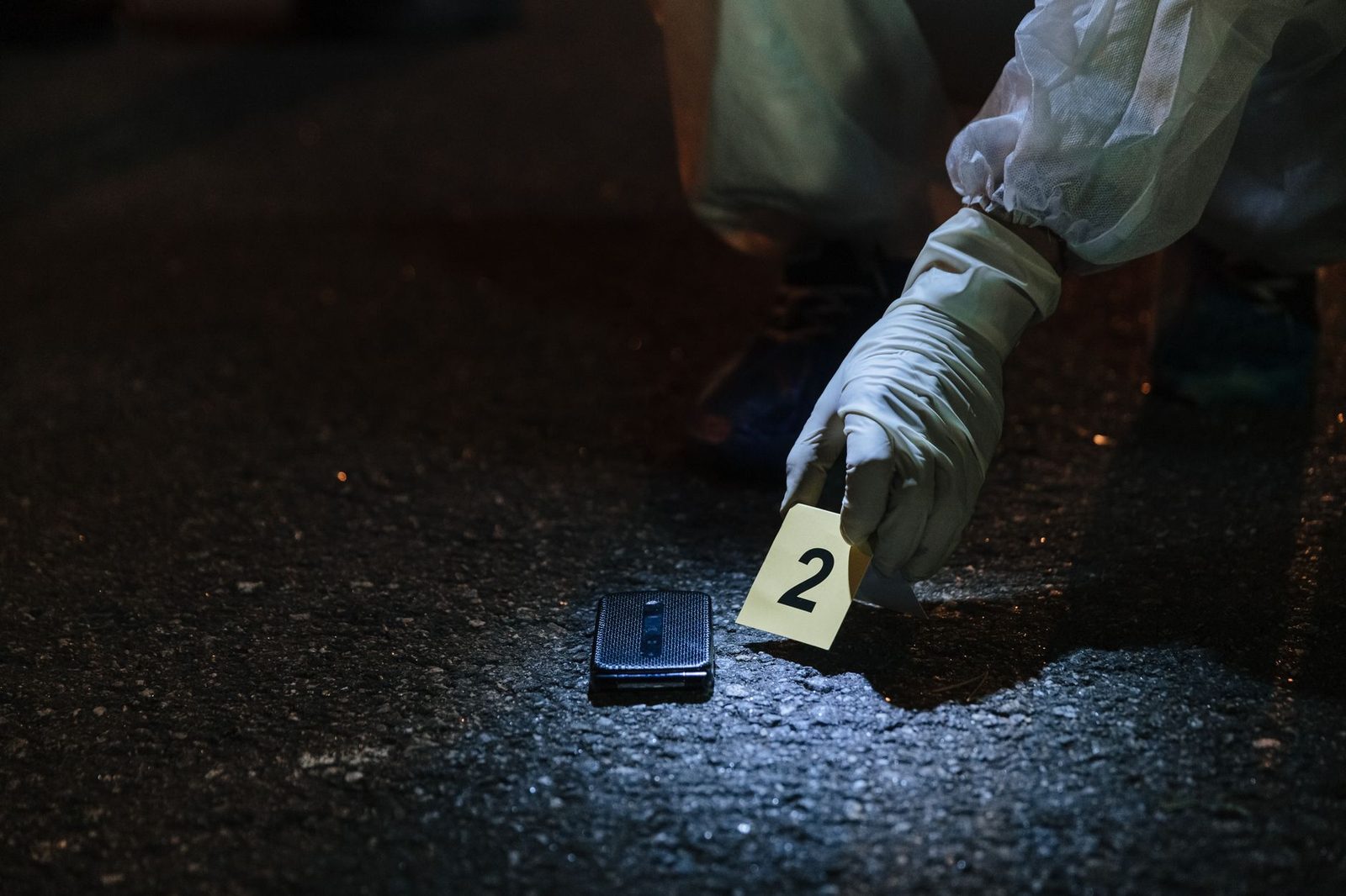 Investigador forense examinando evidencia en una calle urbana nocturna.