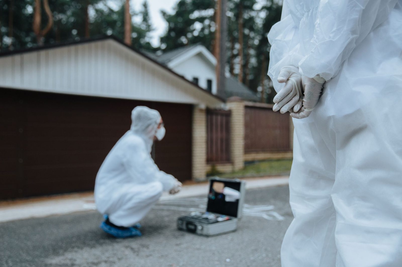 Investigadores forenses en trajes blancos examinan una escena de crimen en área residencial.
