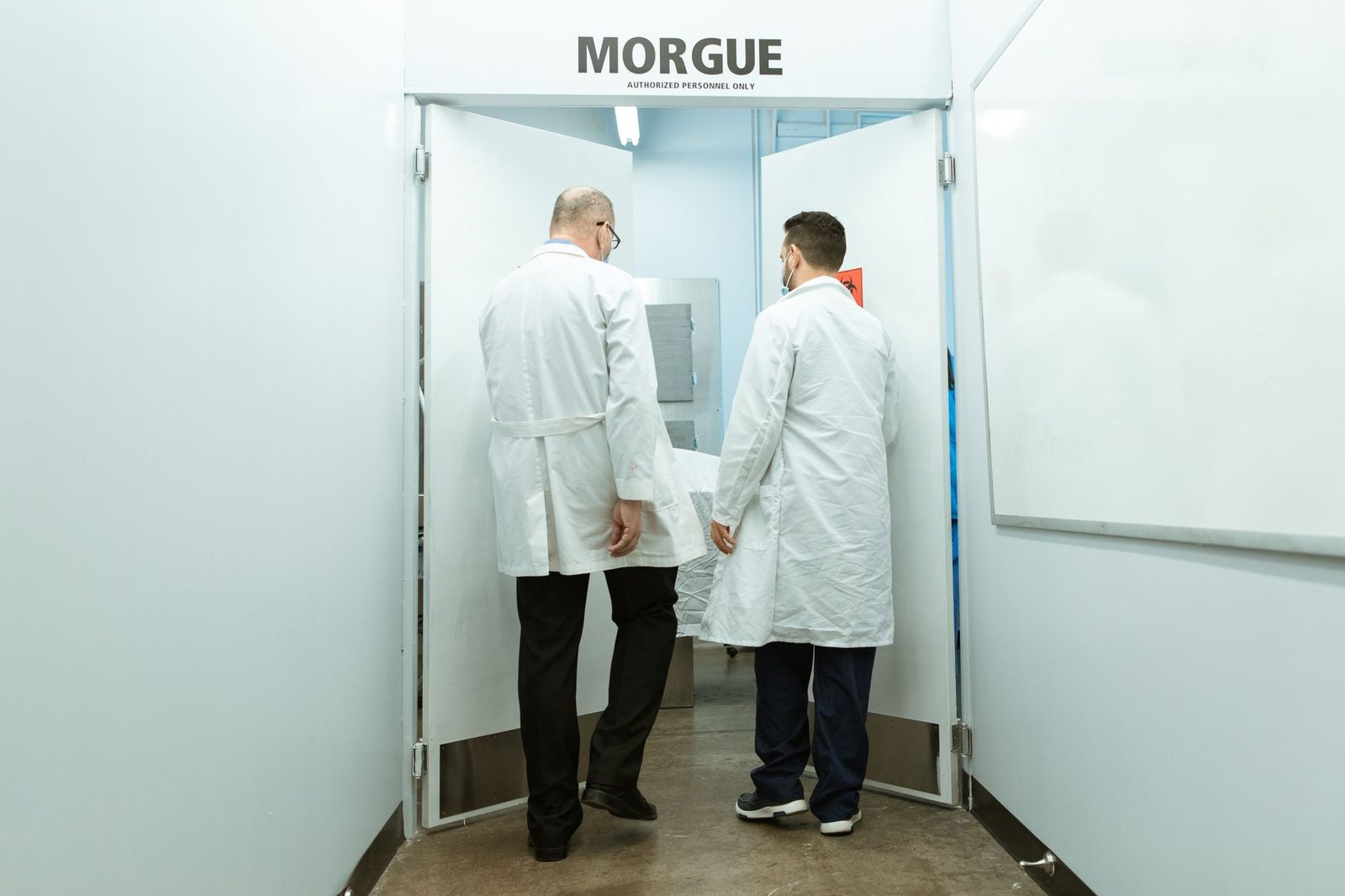 Medical professionals transporting a body on a stretcher into a morgue.