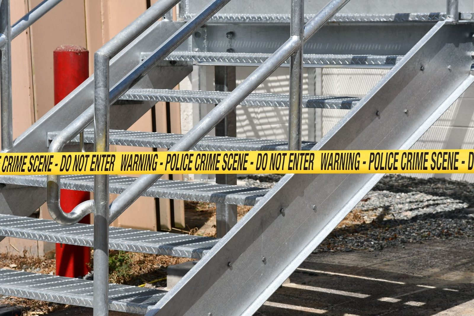 Metal stairway blocked by yellow police crime scene tape outdoors.