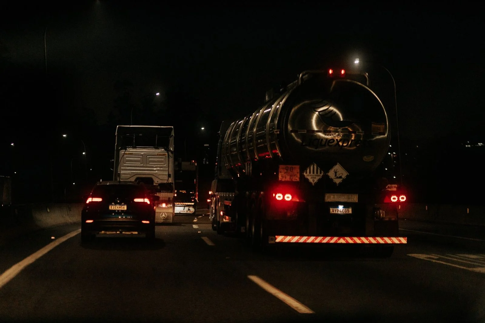 Multiple vehicles on a dark highway at night with headlights illuminated.