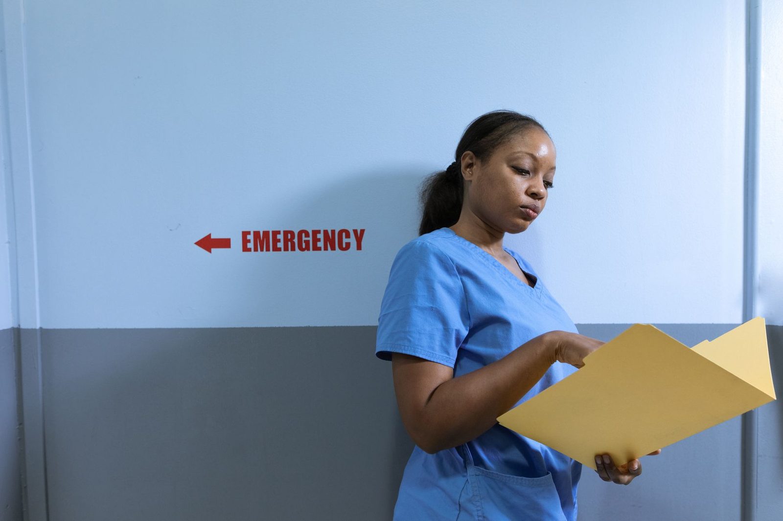 Nurse in blue scrubs reviewing medical records in a hospital emergency room.