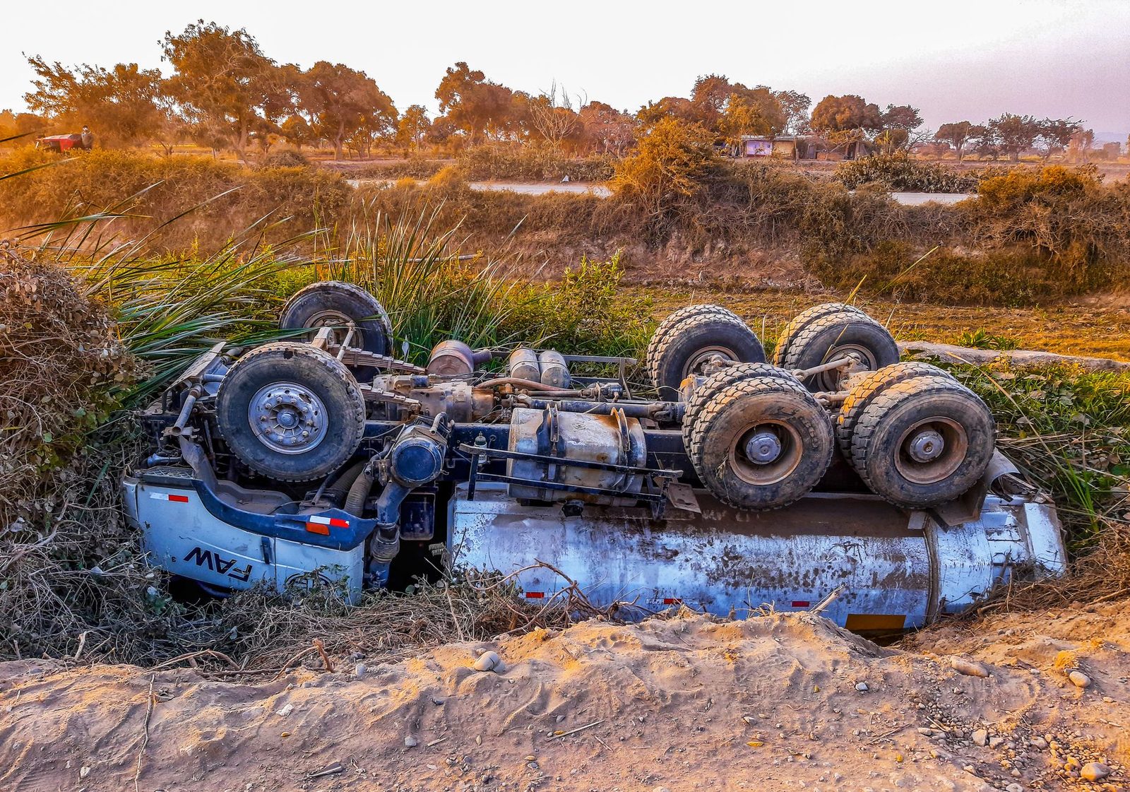 Overturned truck on rural dirt road during daytime.