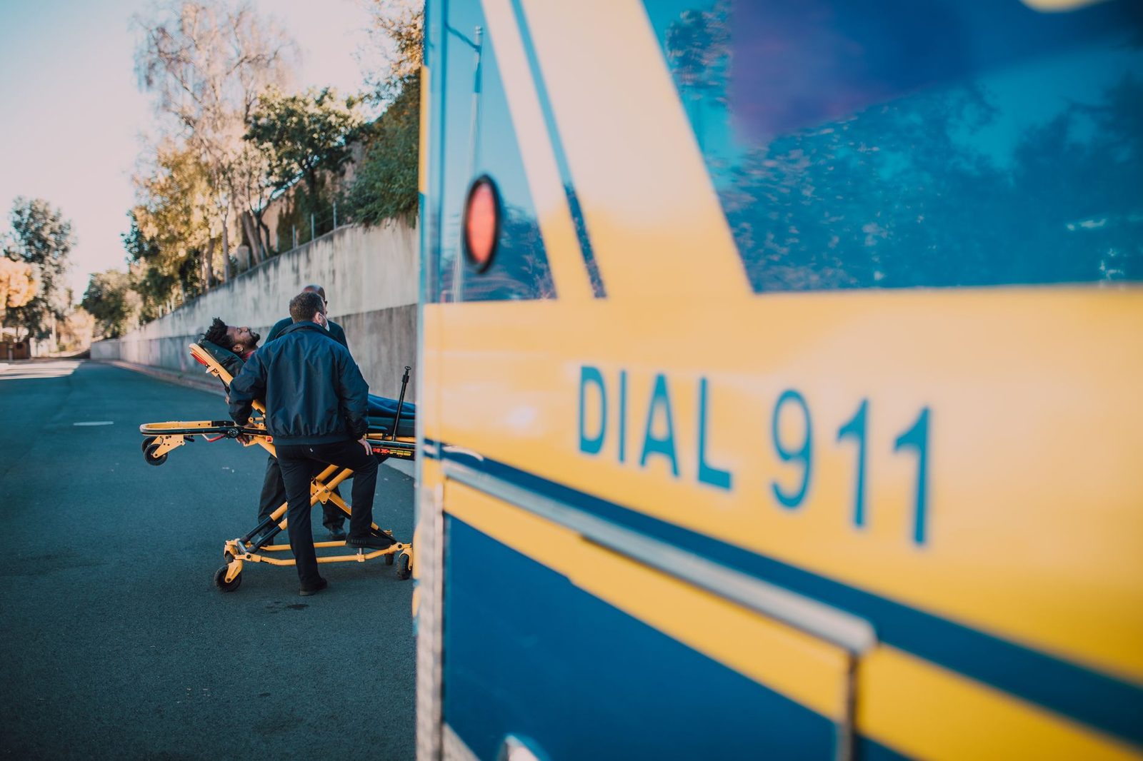 Paramedics loading an injured patient into an ambulance on a sunny day.