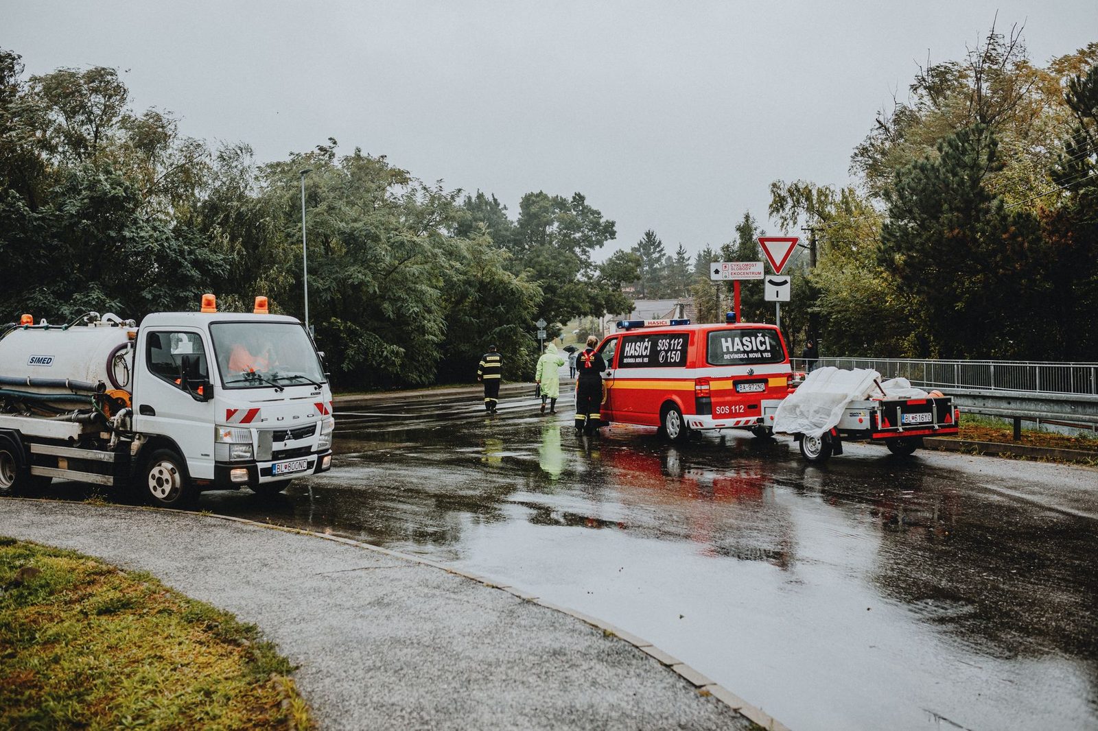 Rescue vehicles and emergency personnel at accident scene on wet road.
