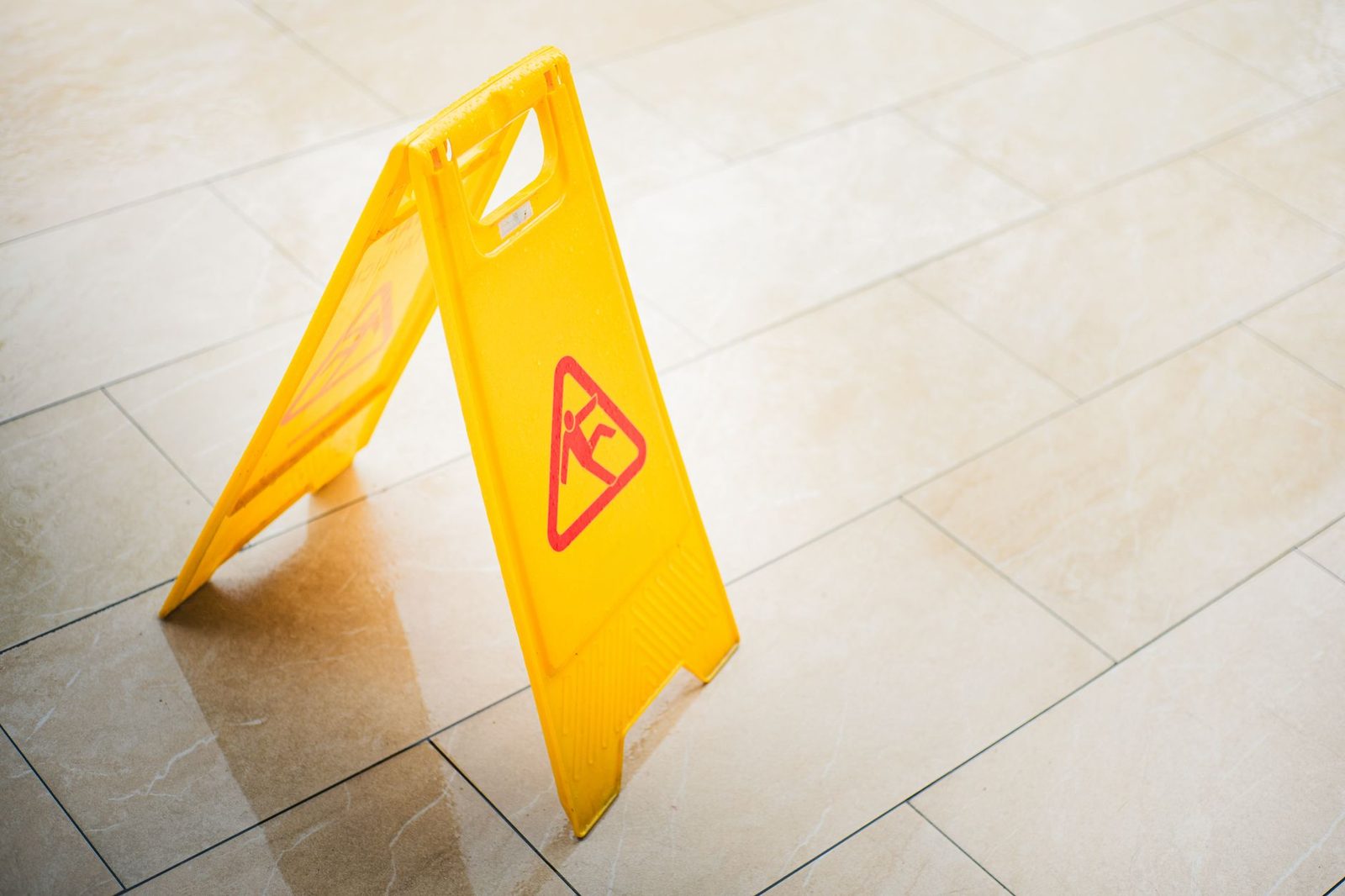 Señal de precaución amarilla en piso mojado advirtiendo sobre peligro de resbalones.