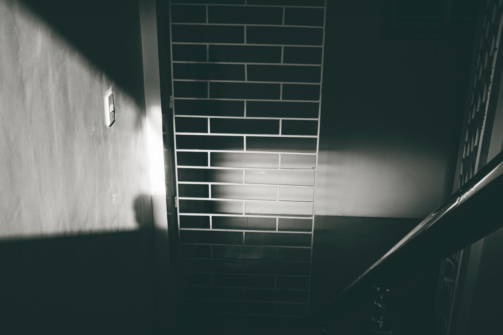 Sombra de persona junto a pasamanos e interruptor de luz en casa iluminada por el sol.