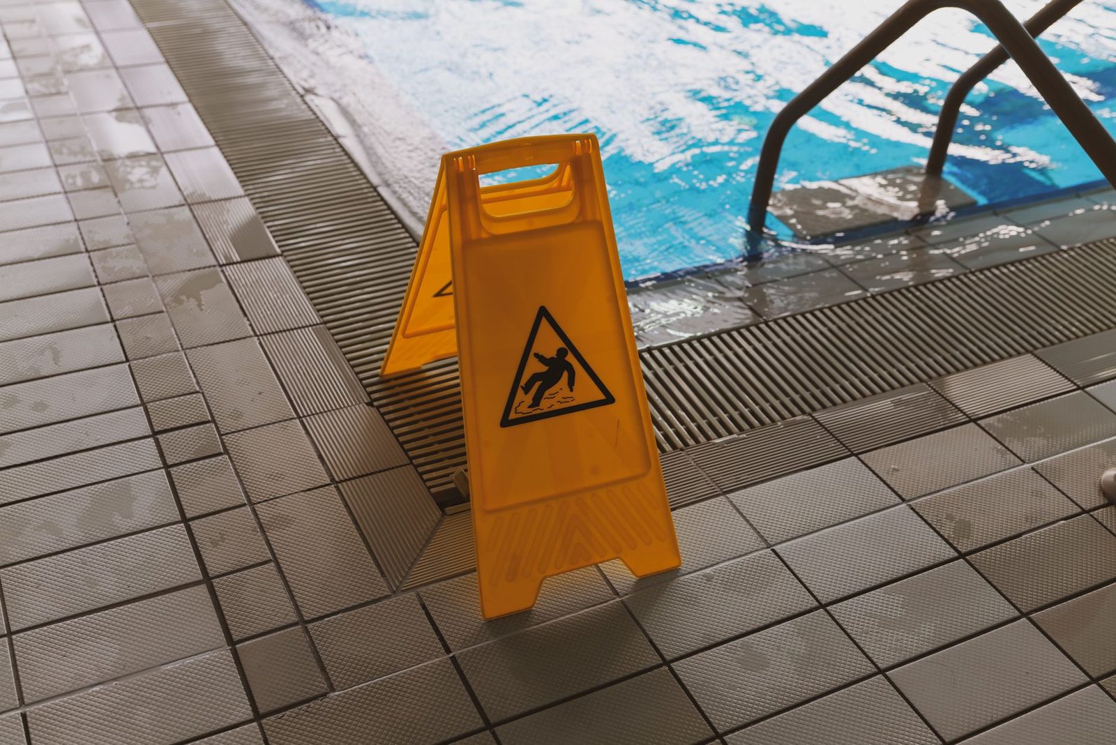 Wet floor caution sign placed beside a swimming pool.