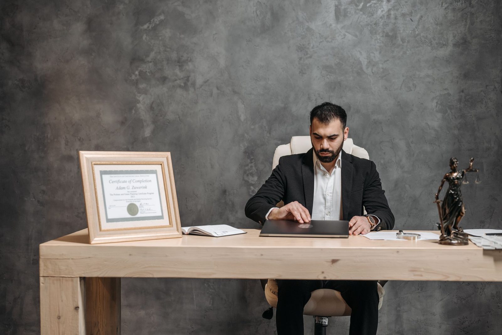 A bearded lawyer sits at a desk in his office, reviewing documents with a focused, professional expression.