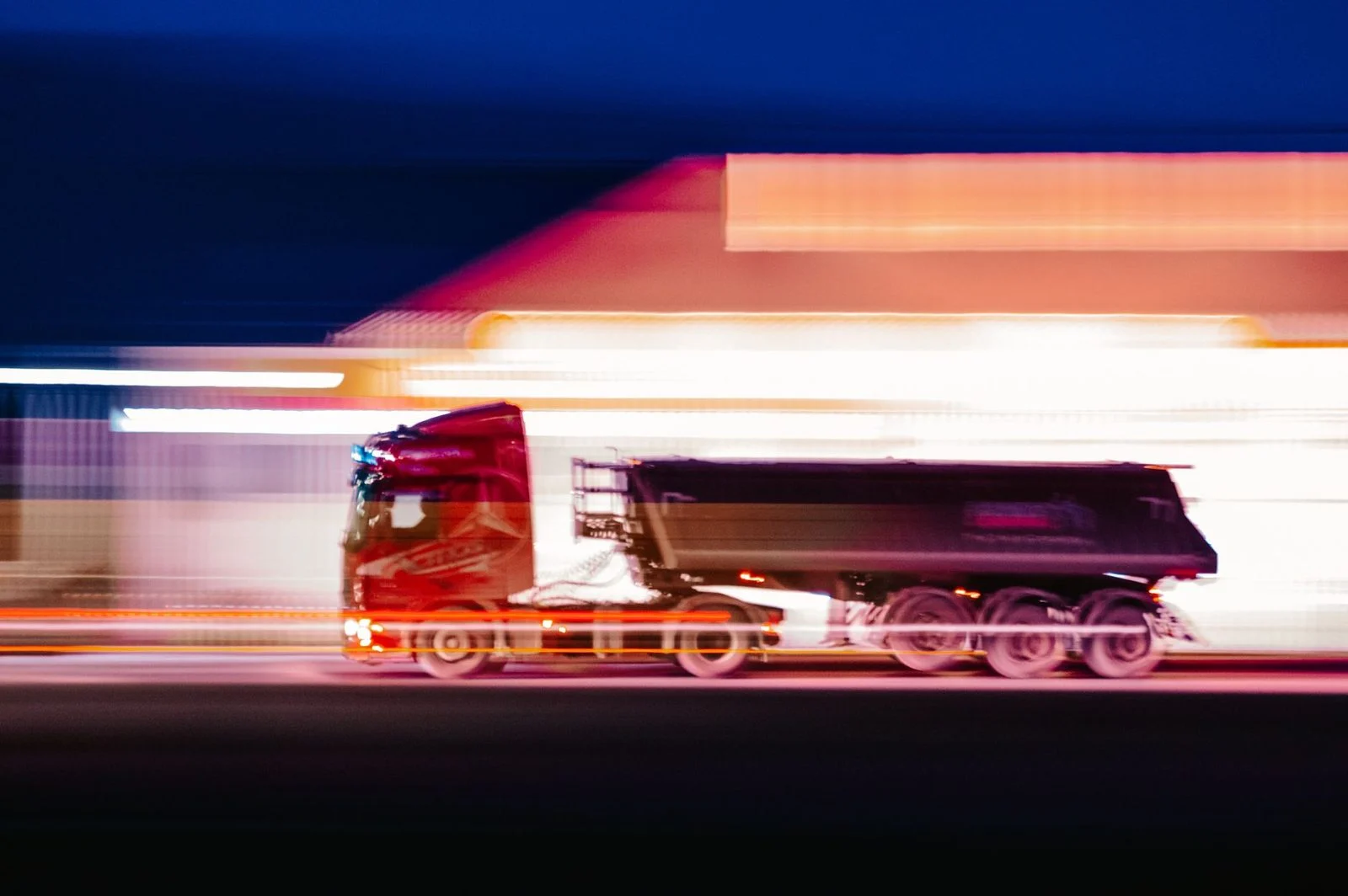 A blurred delivery truck speeds through a city street at night, its lights streaking past.