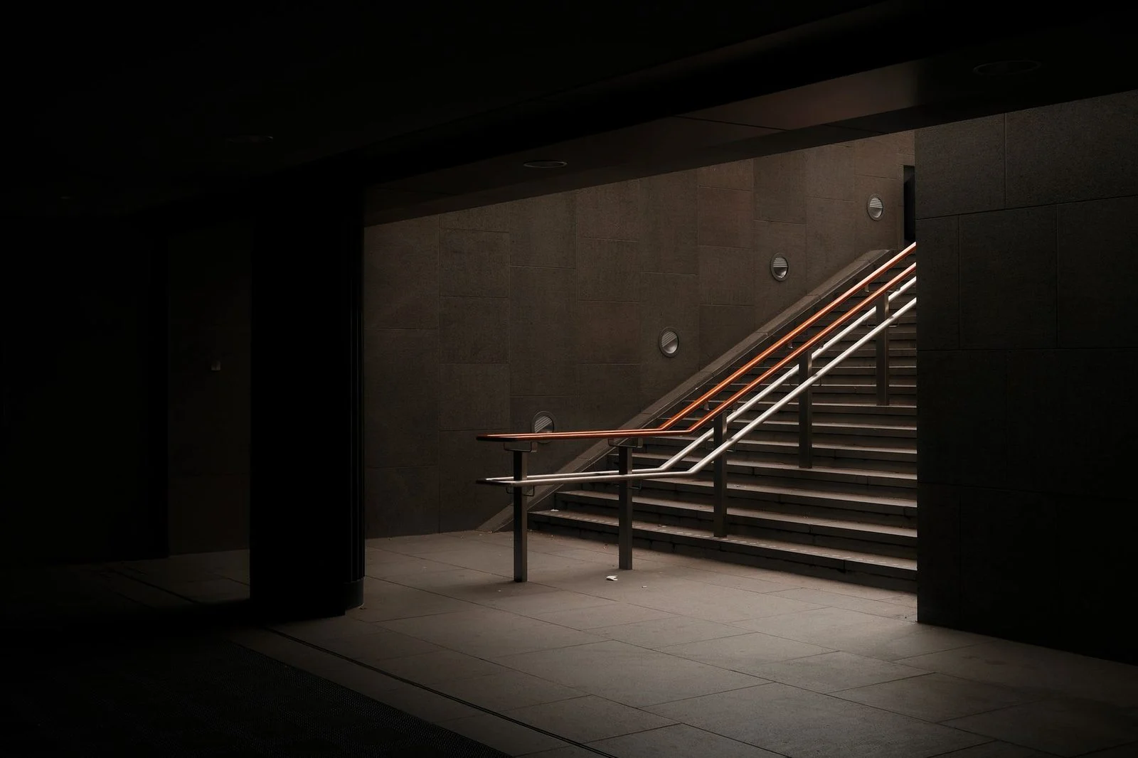Escalera de concreto desgastada y oscura, con barandilla metálica, que desciende hacia las sombras.