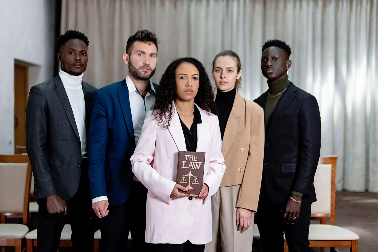 A diverse group of five lawyers stands confidently in an office, one holding a law book.