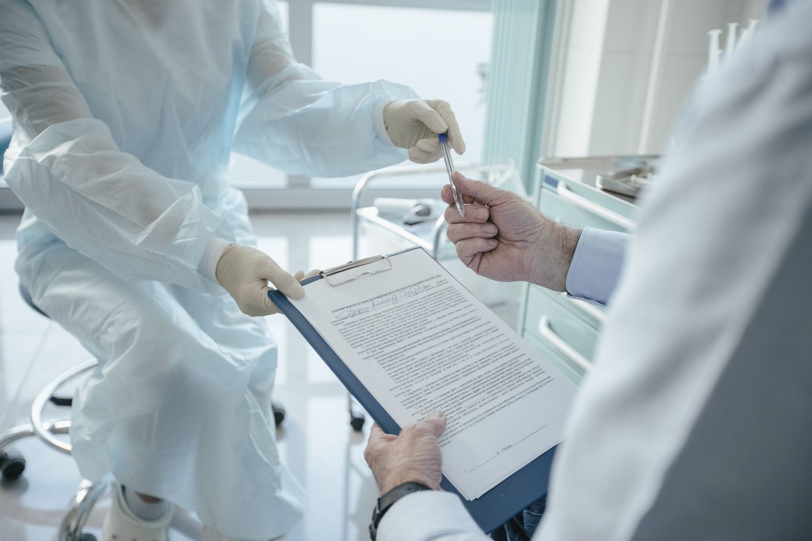 A doctor hands a clipboard to a patient to sign, in a medical setting.