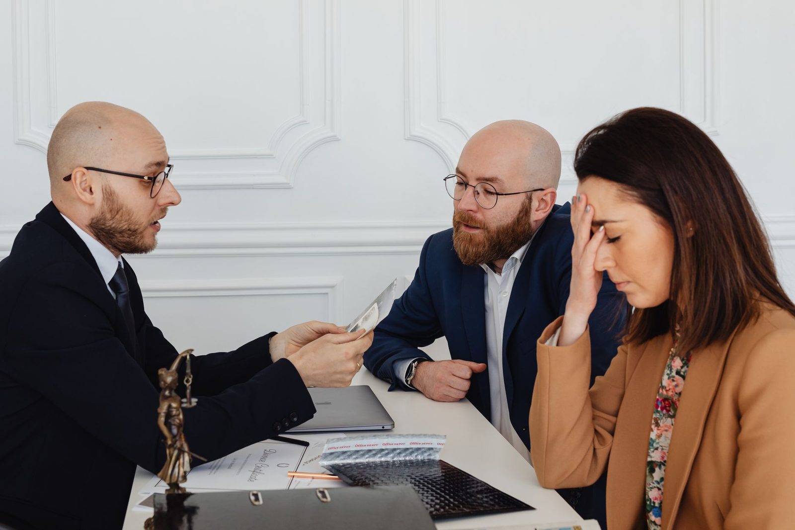 A lawyer sits across from a distressed couple during a tense meeting about a divorce settlement.