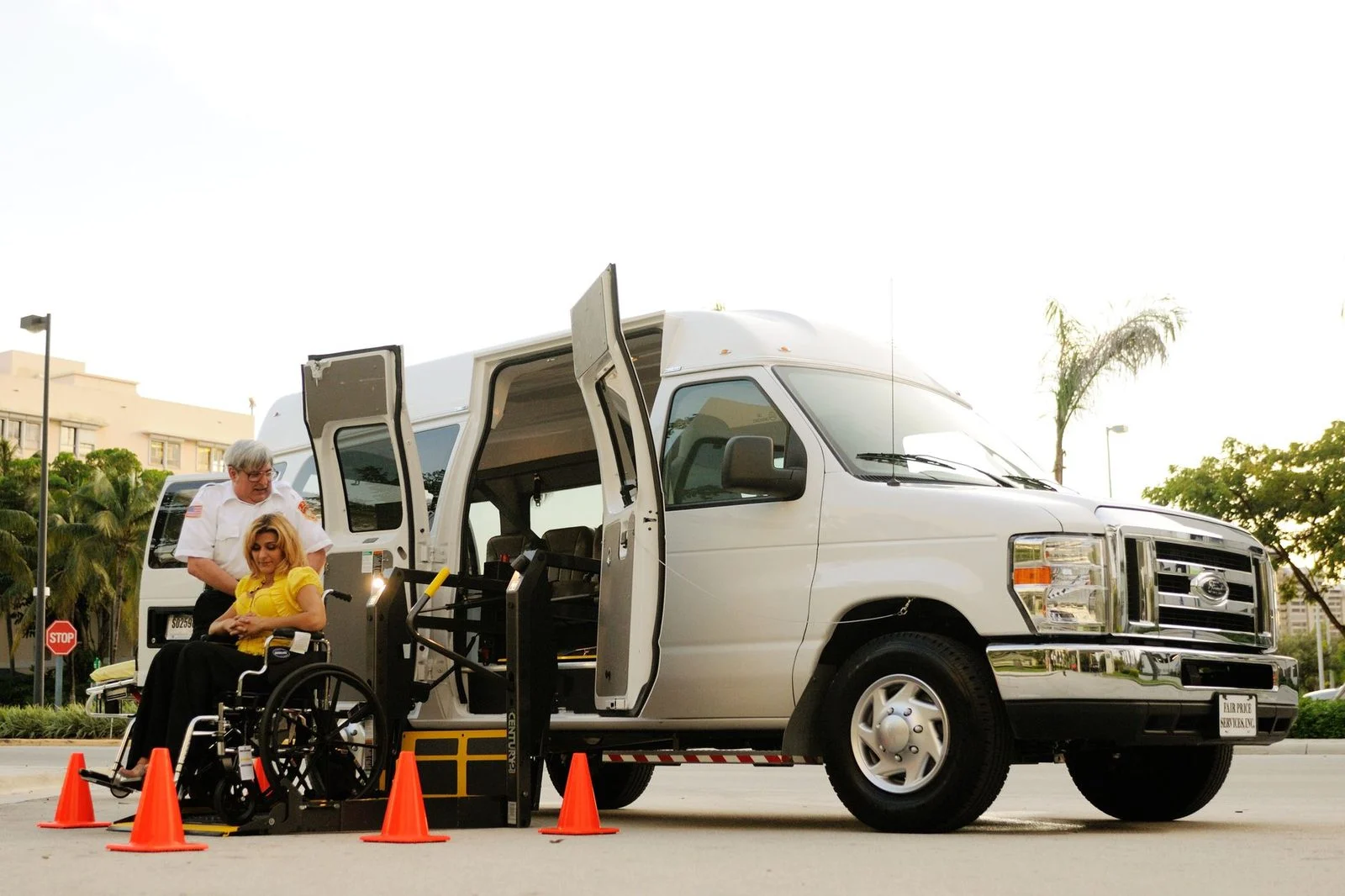 A wheelchair user and an assistant use a ramp to board an accessible transportation van outdoors.