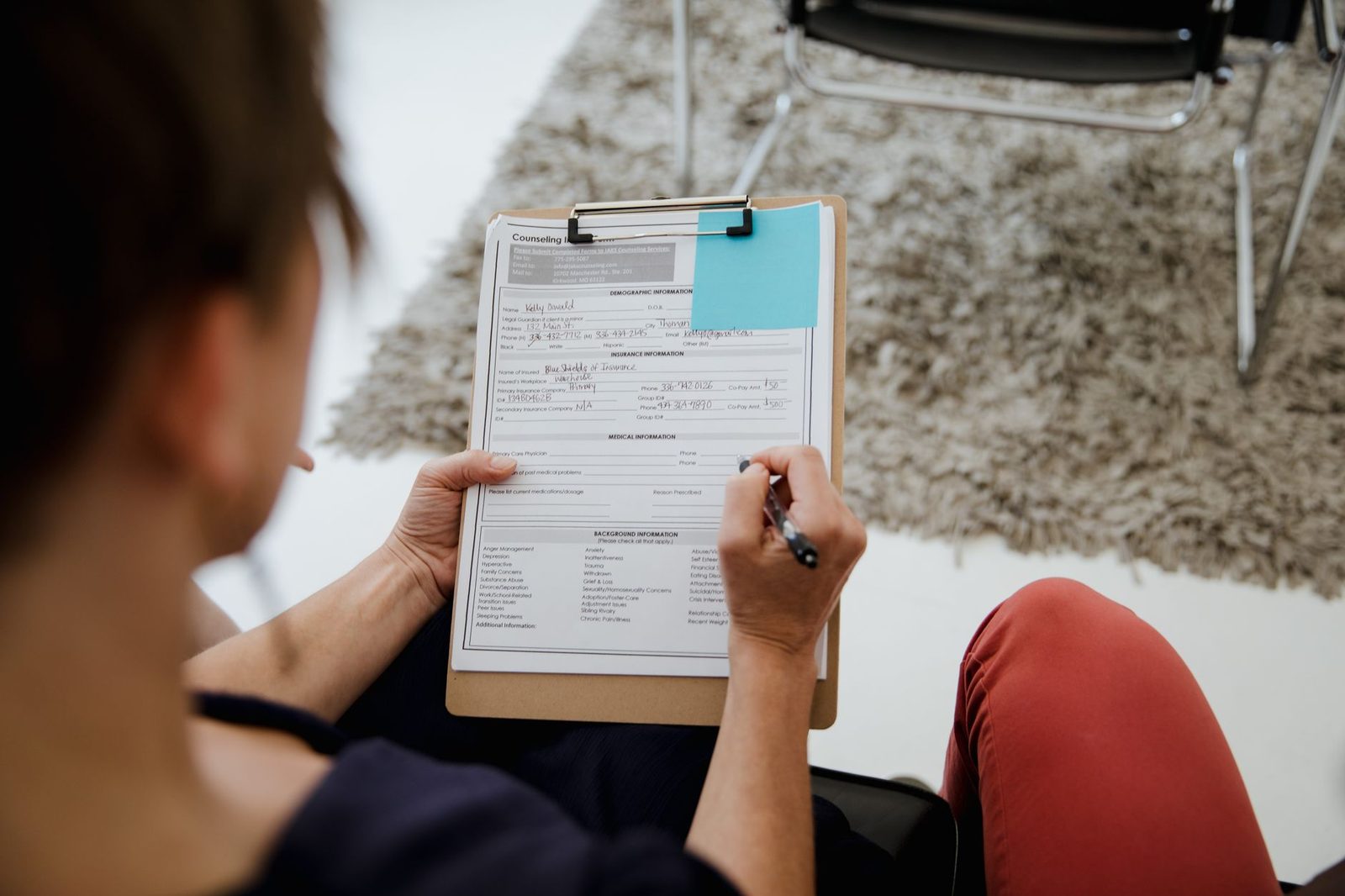 A woman fills out a form at a desk during an office appointment.