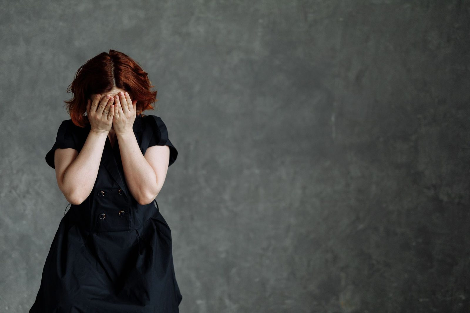 Mujer con vestido negro, de pie junto a una pared de hormigón, con expresión triste y tensa.