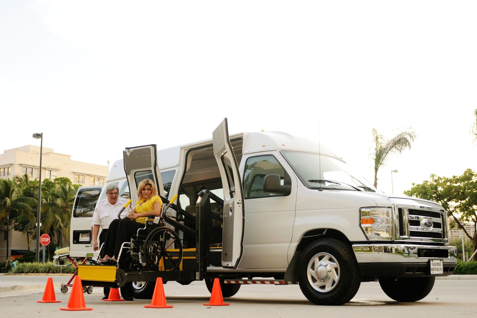 A woman in a wheelchair boarding an accessible van via a lift while a driver assists.