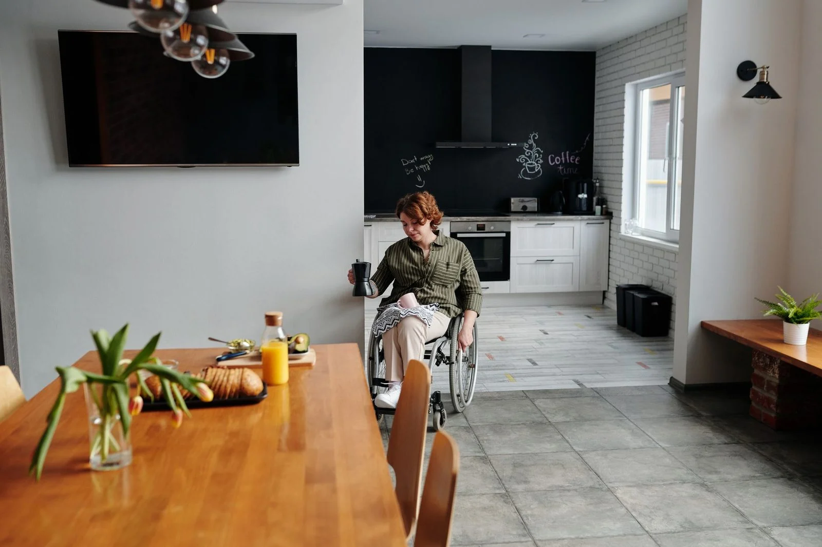 Mujer en silla de ruedas sostiene una taza de café en una cocina moderna.