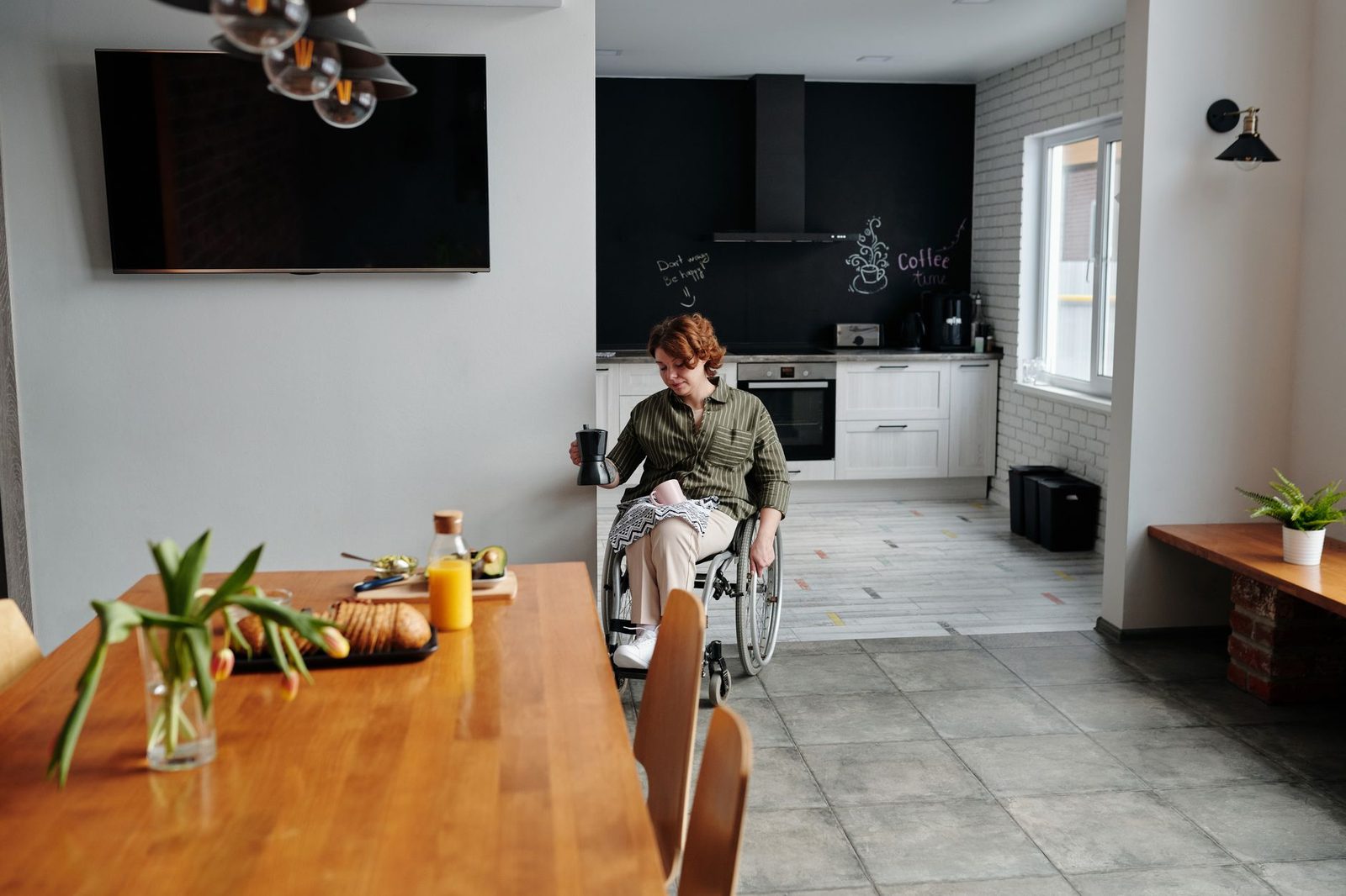 A woman in a wheelchair holds a cup of coffee in a modern kitchen.
