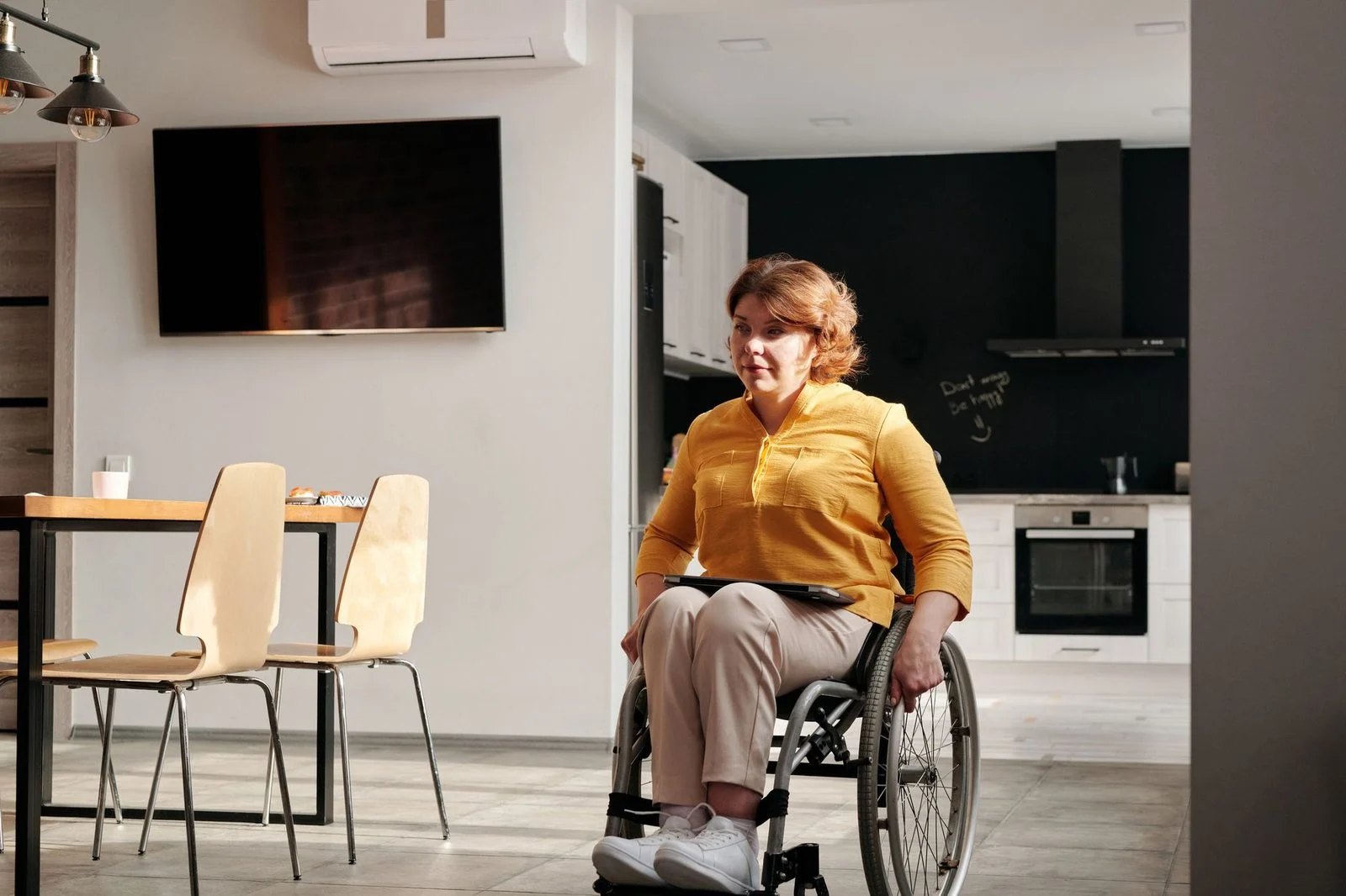 Una mujer en silla de ruedas sonríe mientras cocina en una cocina accesible con encimeras bajas.