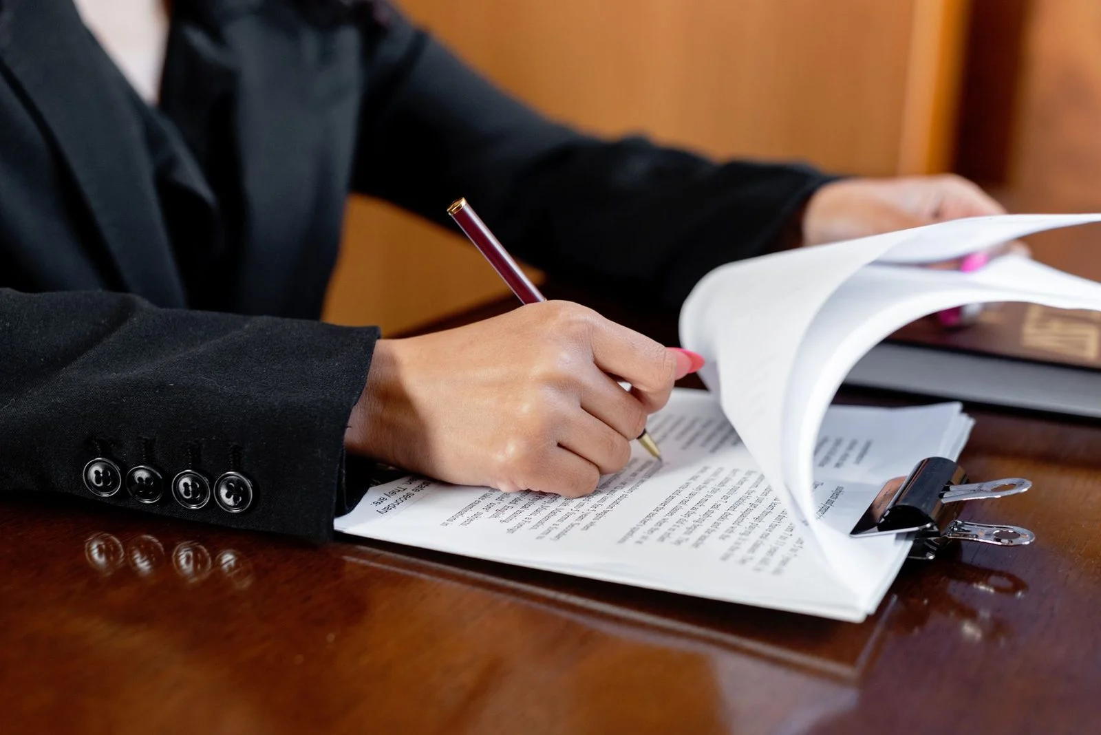 A woman signs legal documents with a pen at a desk in an office.