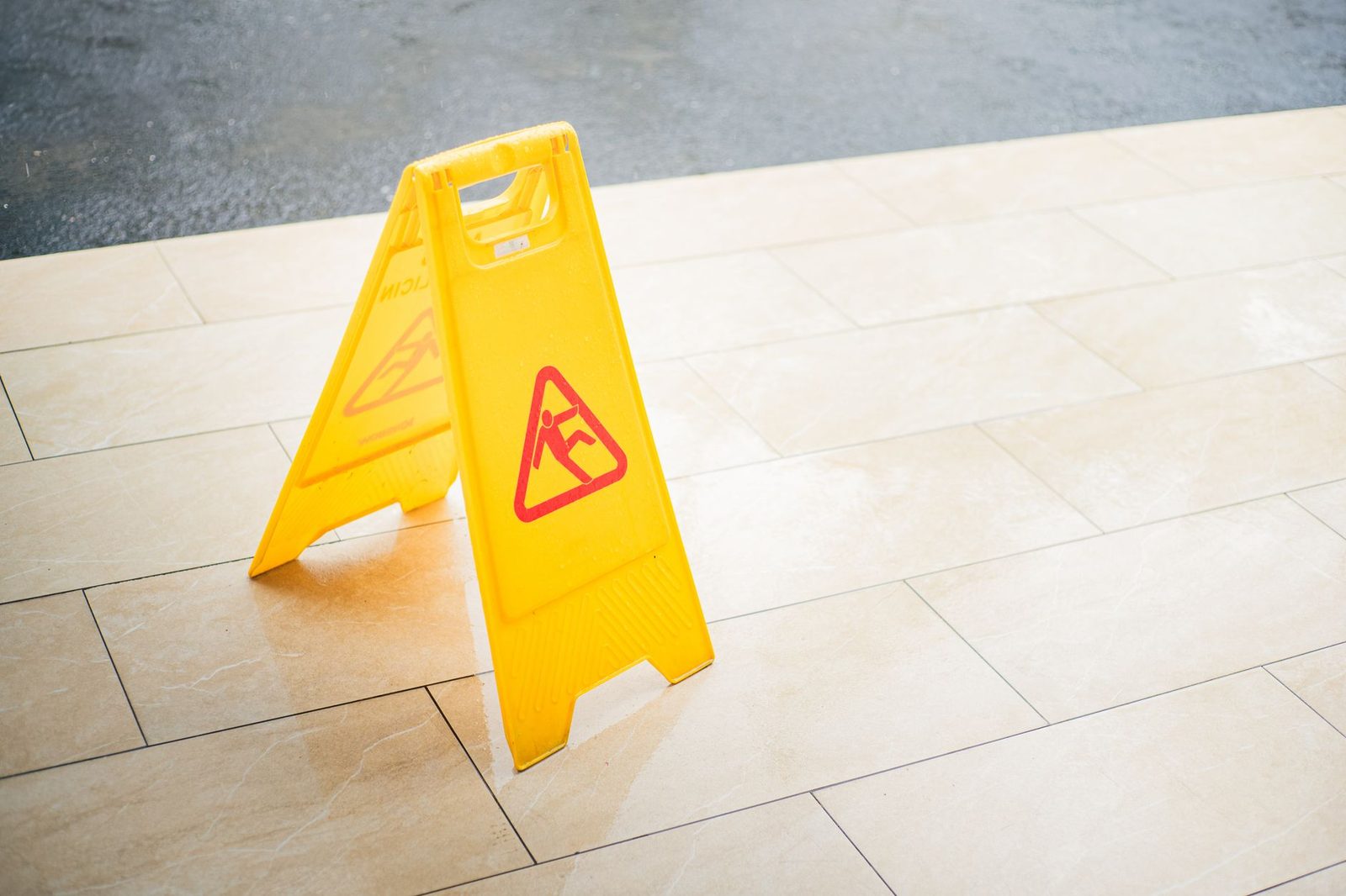 Un letrero amarillo de precaución sobre un suelo de baldosas, que señala una zona mojada.