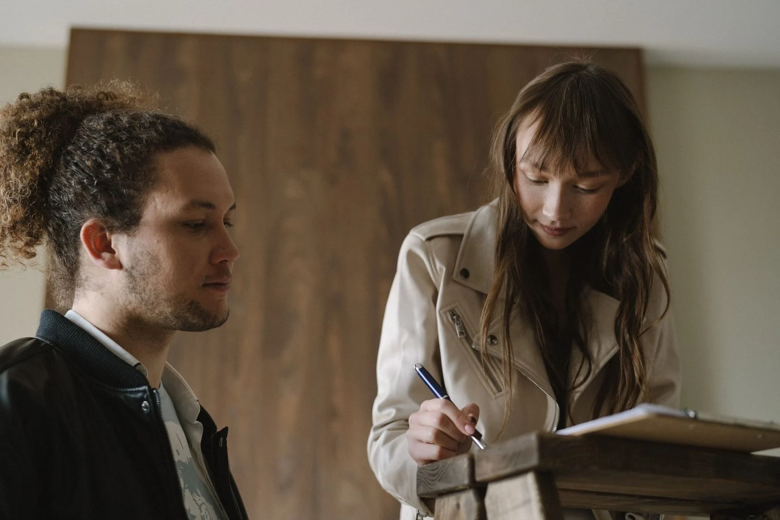 A young couple reviews and signs documents at a table indoors.