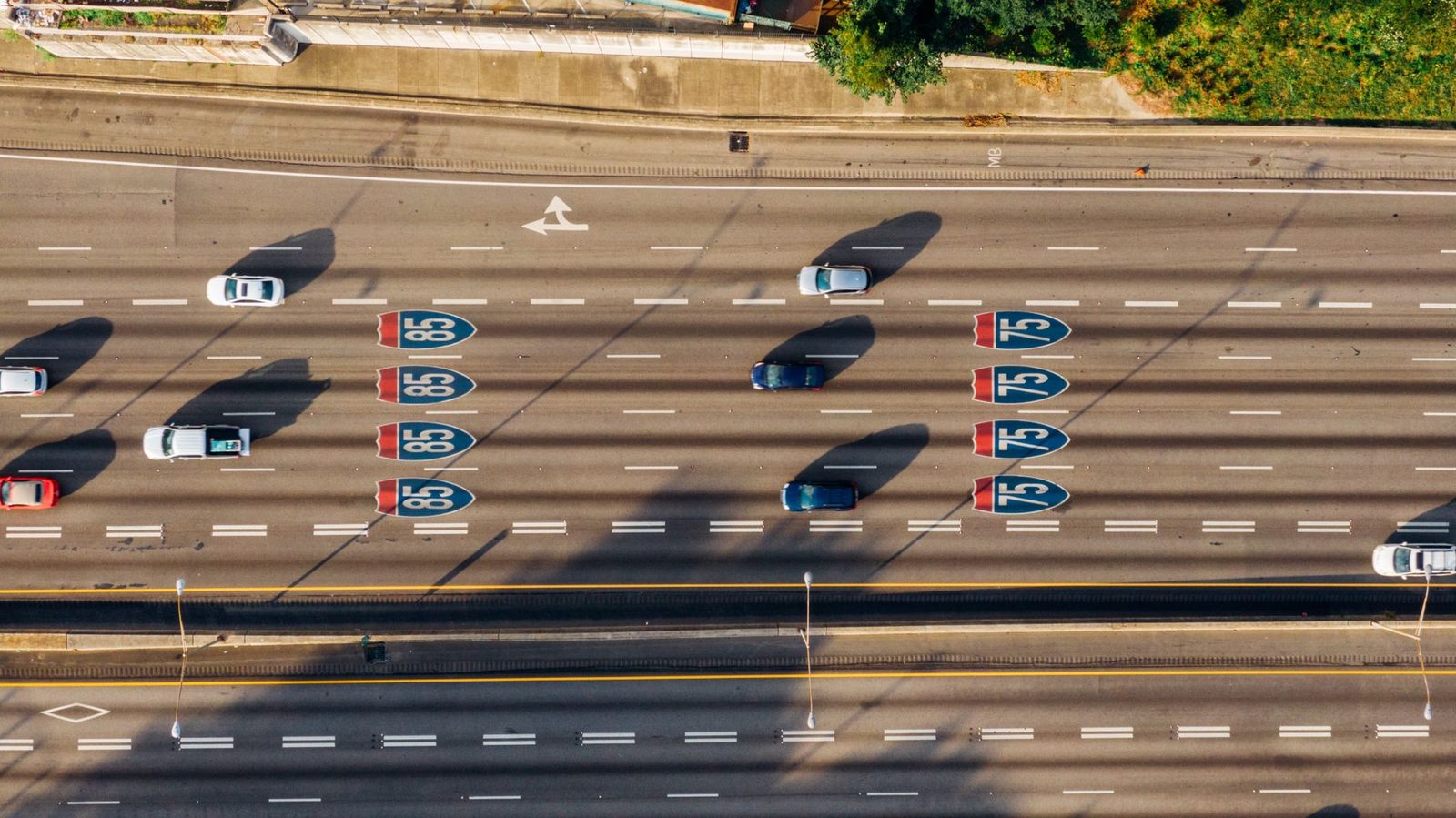 Aerial view of multiple cars driving on Atlanta's I-85 and I-75 highways on a sunny day.