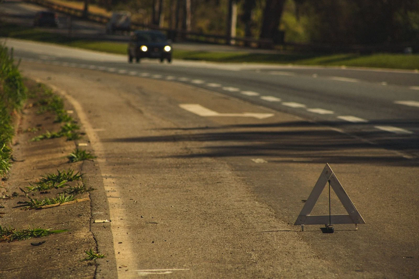 Automóvil con faros encendidos en carretera con señal de alerta al atardecer.