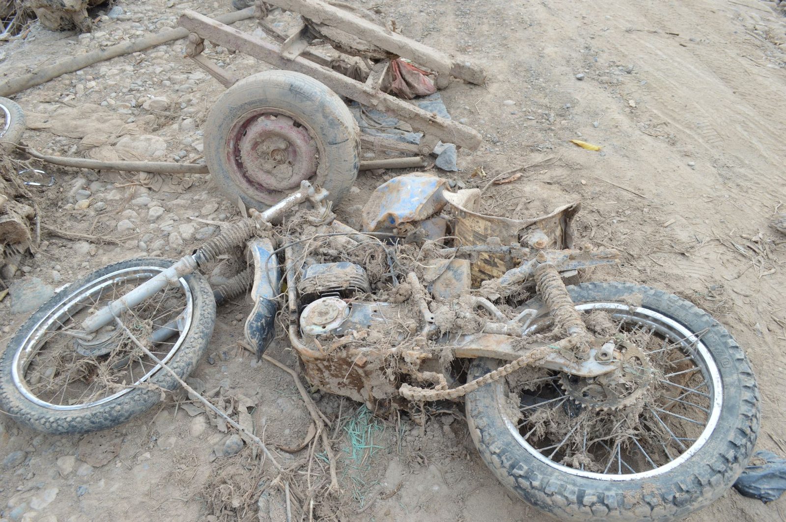 Motorcycle with broken parts, covered in mud and debris, sitting in disrepair.
