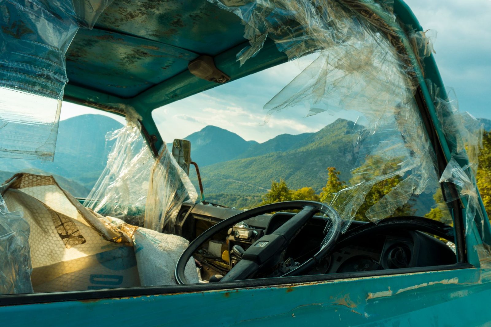 Camión oxidado y deteriorado con ventanas rotas frente a montañas.