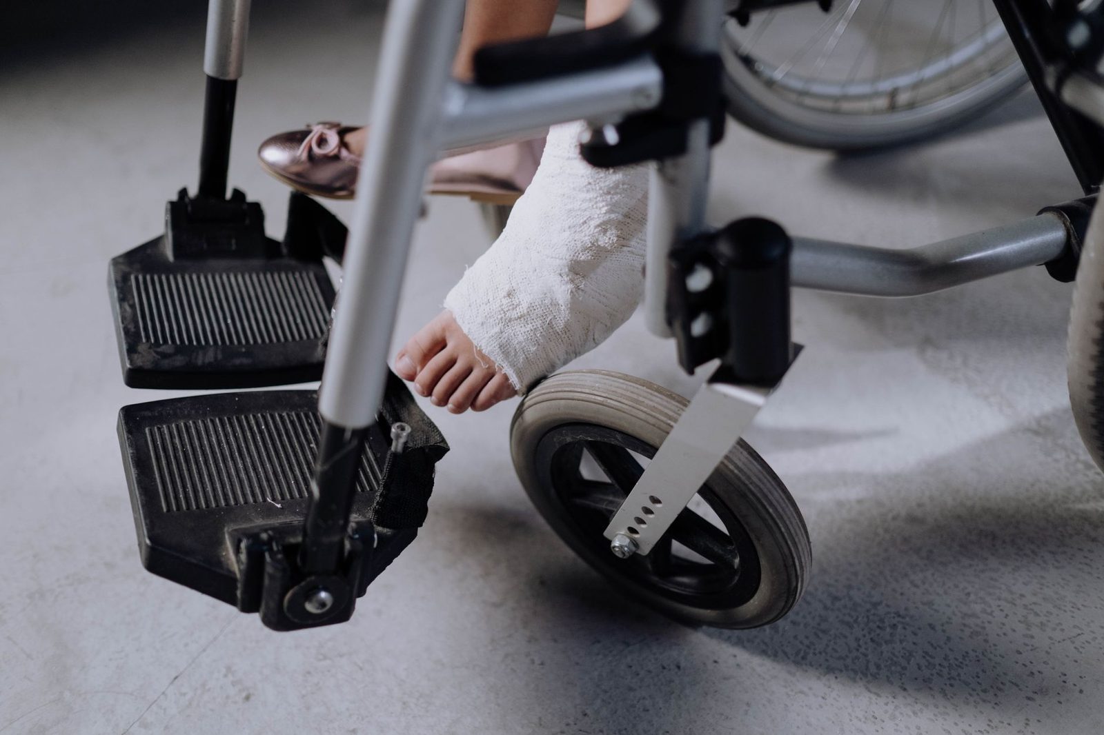 Close-up of a foot in a white cast resting on a wheelchair footrest indoors.