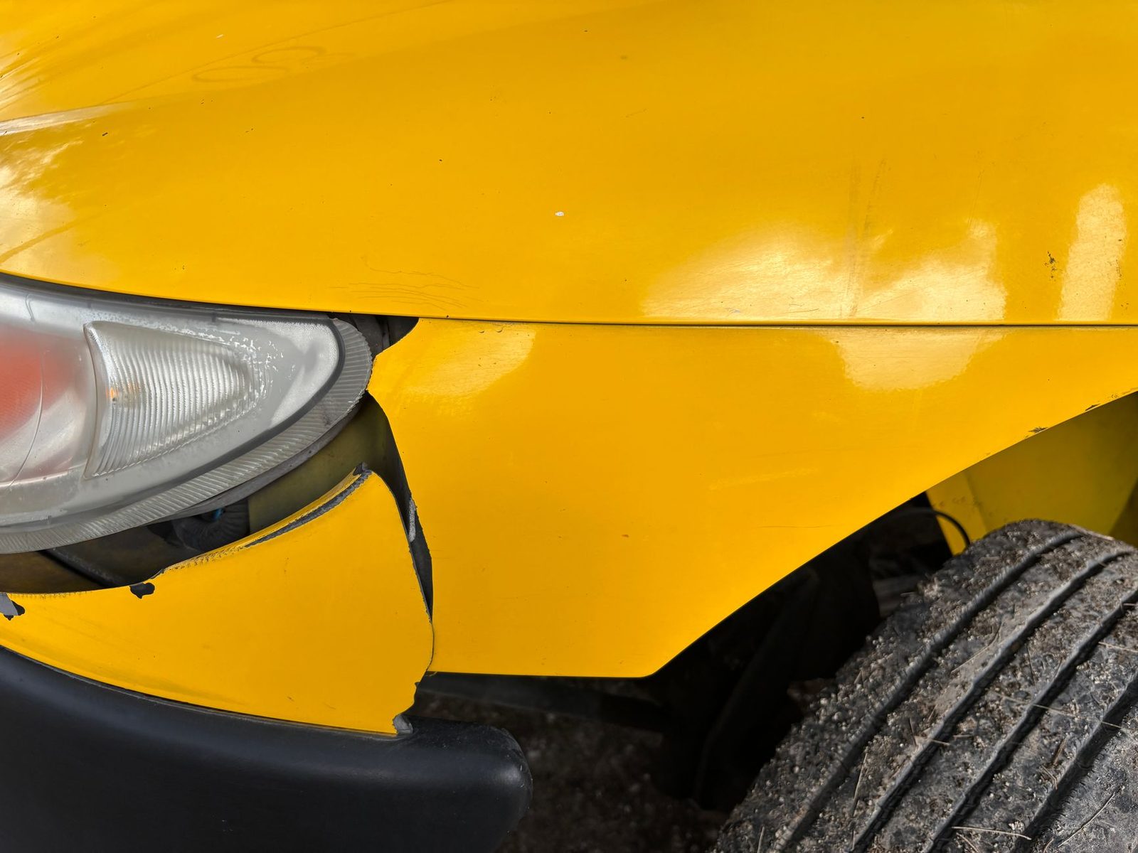 Parachoques delantero abollado y faro agrietado de un coche amarillo tras una colisión.