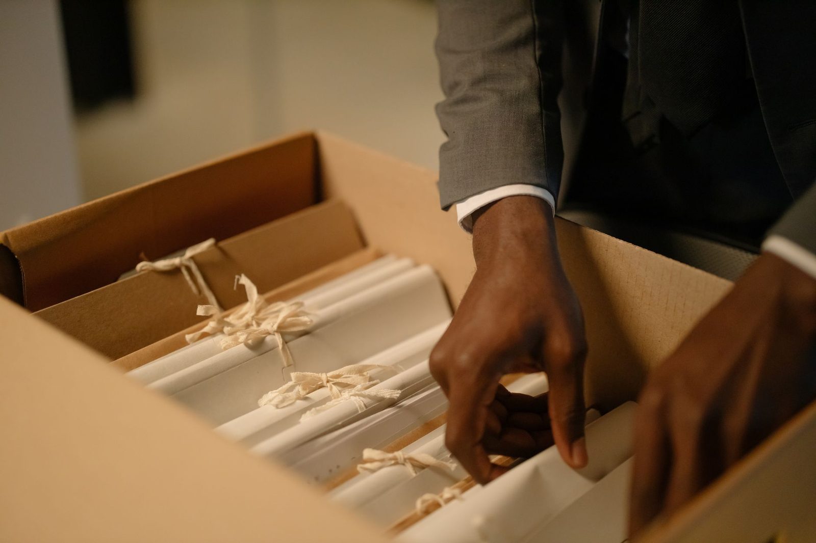 Manos ordenando documentos atados con cinta dentro de una caja de cartón.
