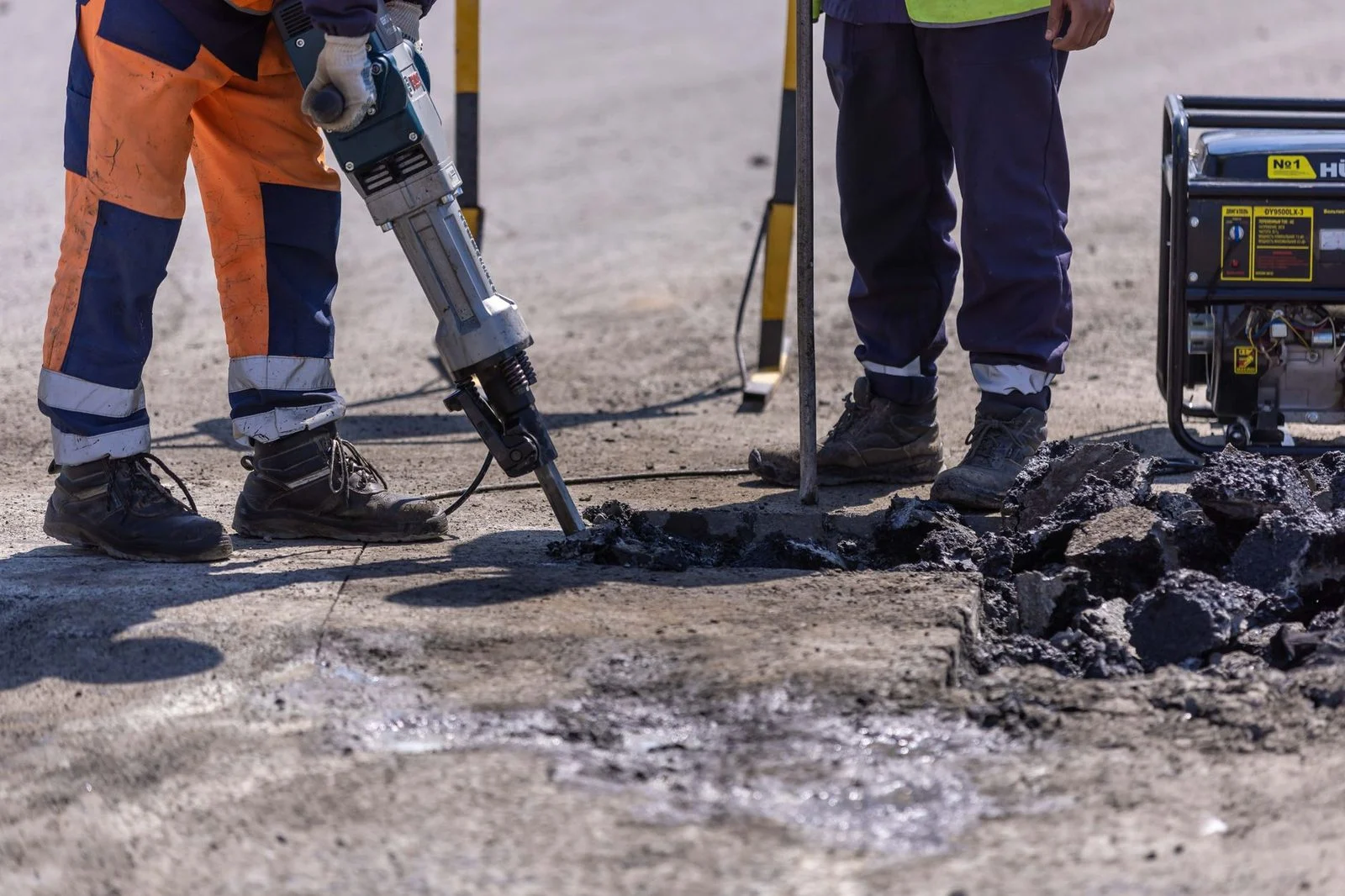 Trabajadores de la construcción usan un martillo neumático para romper asfalto durante obras viales.