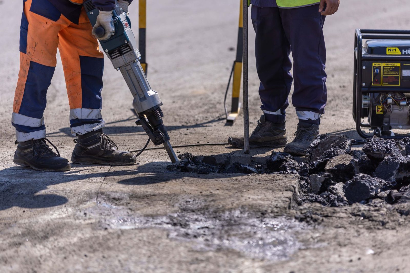 Construction workers using a jackhammer to break up asphalt during road work.