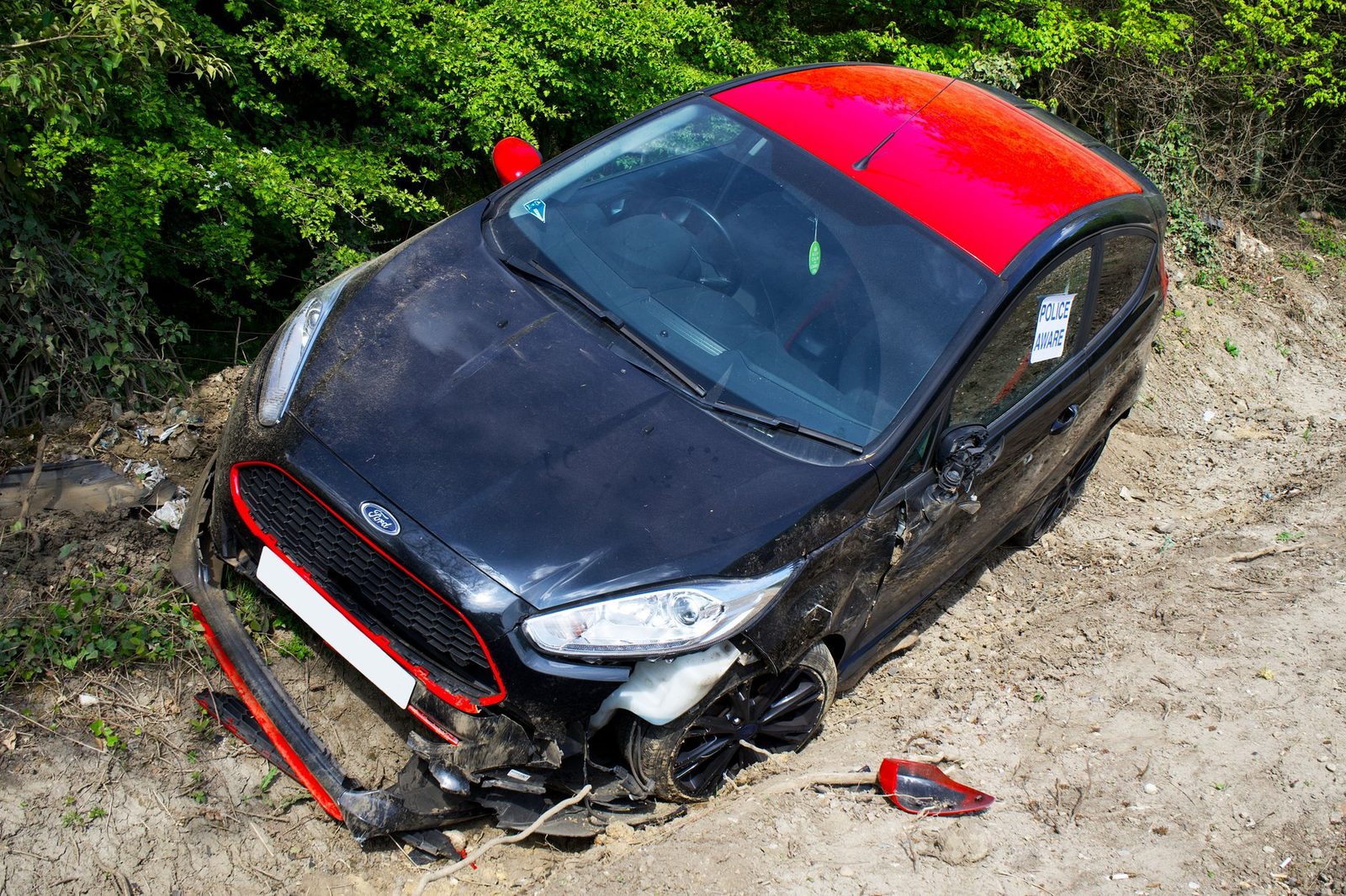 Damaged black and red Ford Fiesta abandoned off-road after collision.