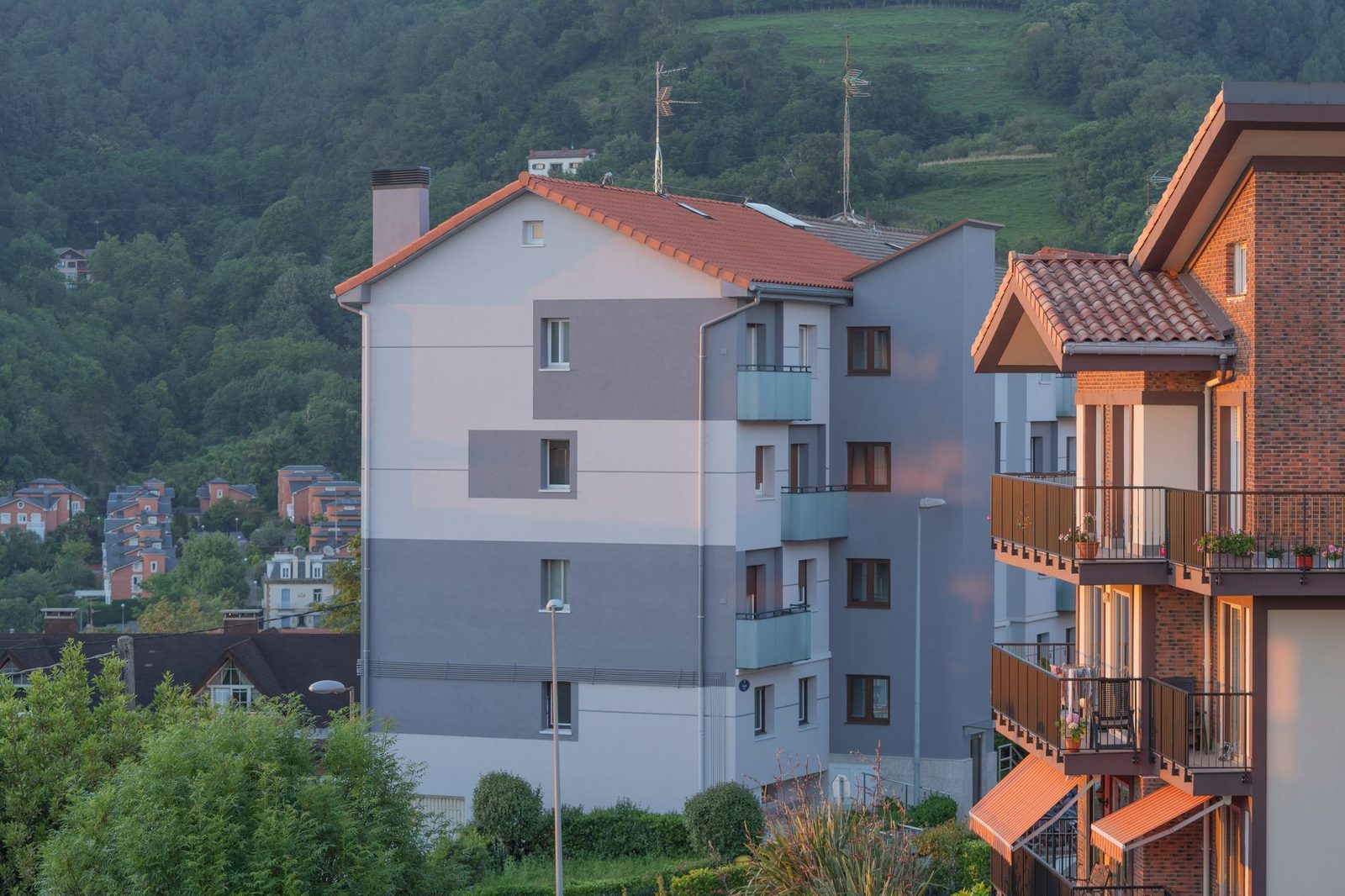 Edificios residenciales con colina verde al fondo al atardecer.